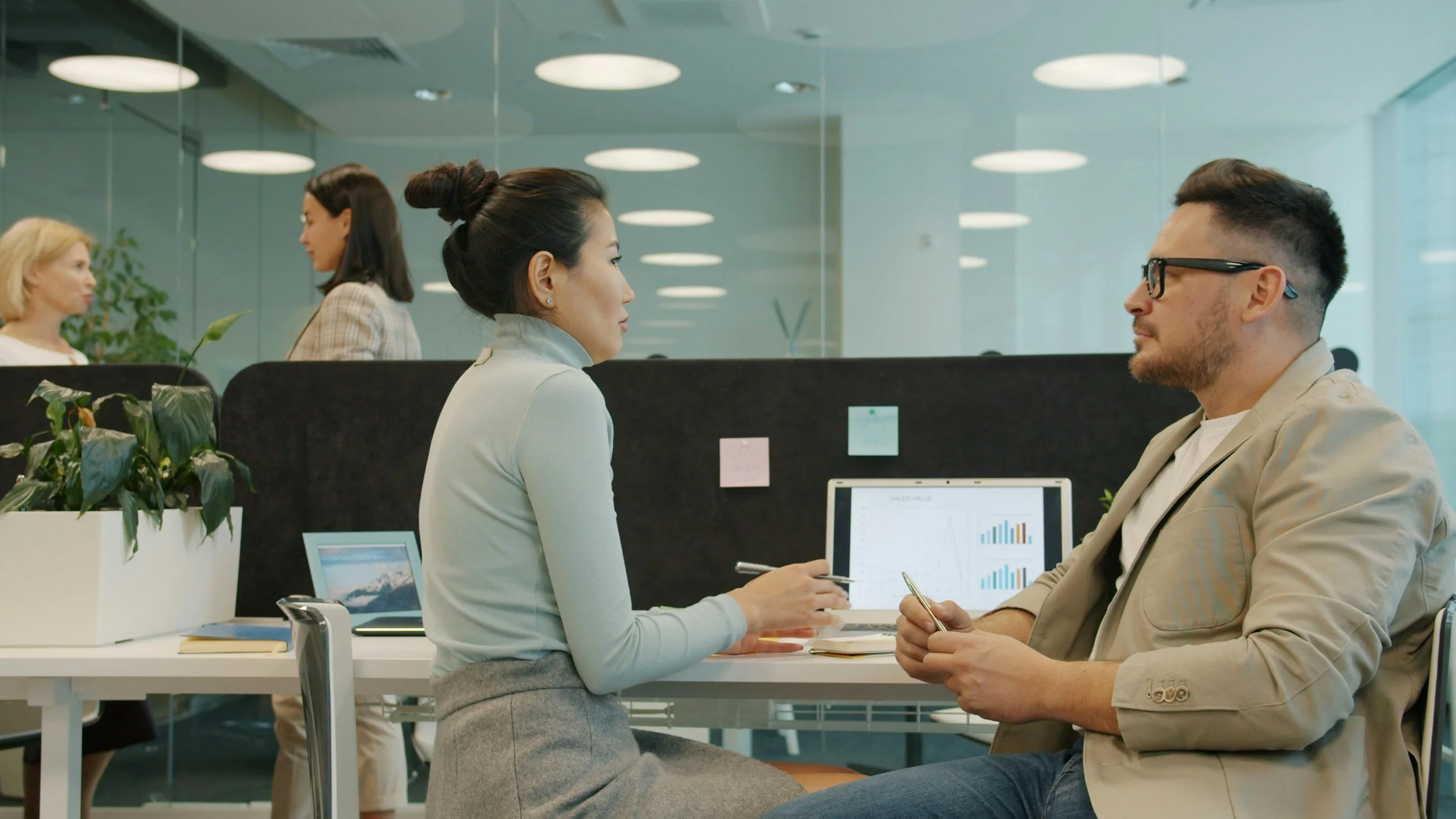 Two office professionals having a focused discussion at a desk in a modern open office.