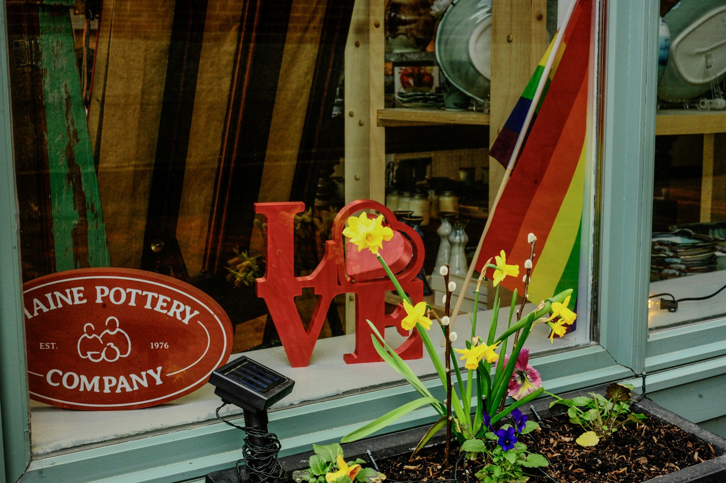 Pride flag displayed outside a local business alongside a love sign, representing year-round support, inclusion, and allyship for the LGBTQIA+ community.