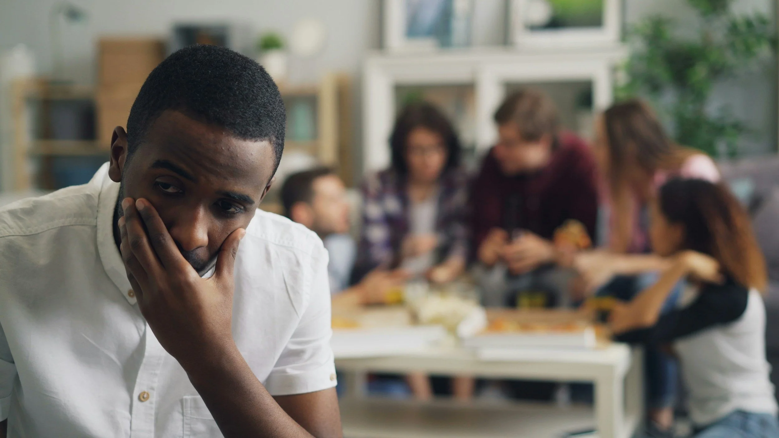 A man looking overwhelmed while family members talk in the background, illustrating the stress, emotional triggers, and difficult family dynamics that can surface during family gatherings.
