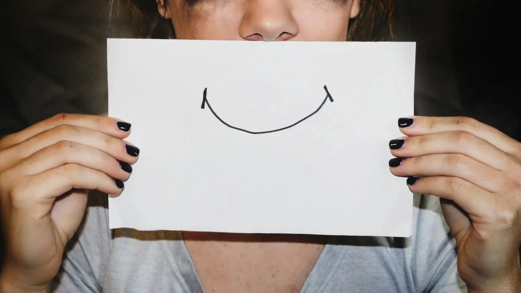 Person holding a paper with a drawn smile in front of their face, illustrating the difference between hiding emotions and taking responsibility for them.