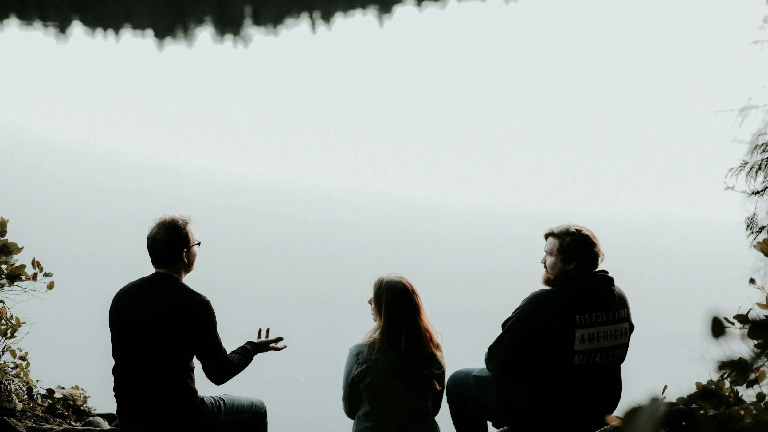 The silhouettes of three people having a conversation while sitting near a cliff-edge, overlooking nature.