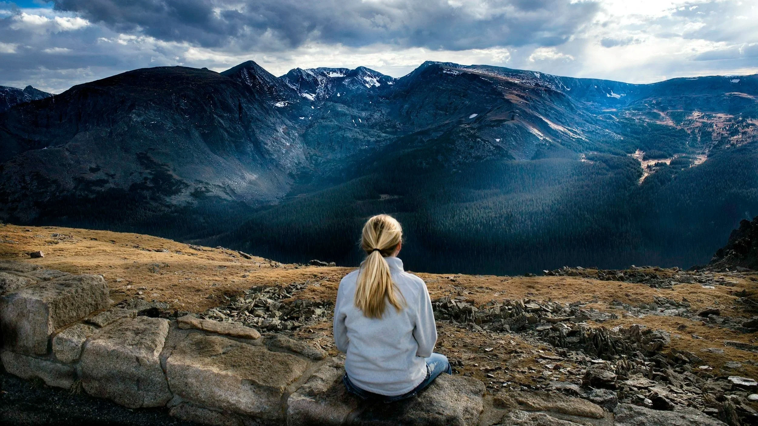 A woman sitting alone outside looking at a large mountain range.