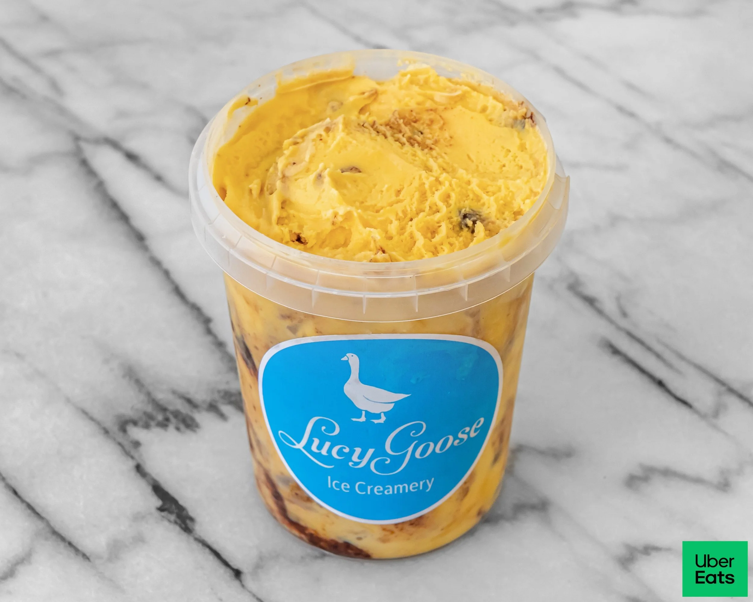 A cup of Lucy Goose ice cream with yellow and chocolate swirls on a marble surface.