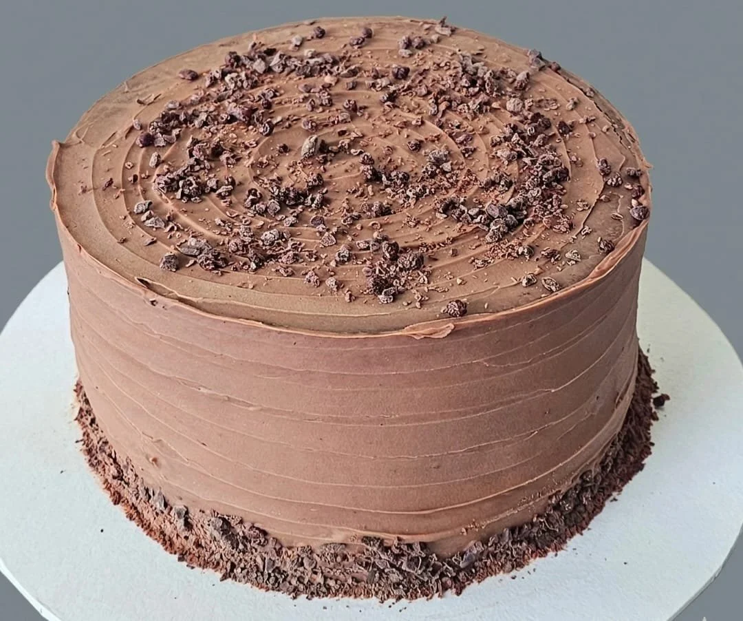 Chocolate cake with swirl icing and chocolate sprinkles on top, sitting on a white cake board.