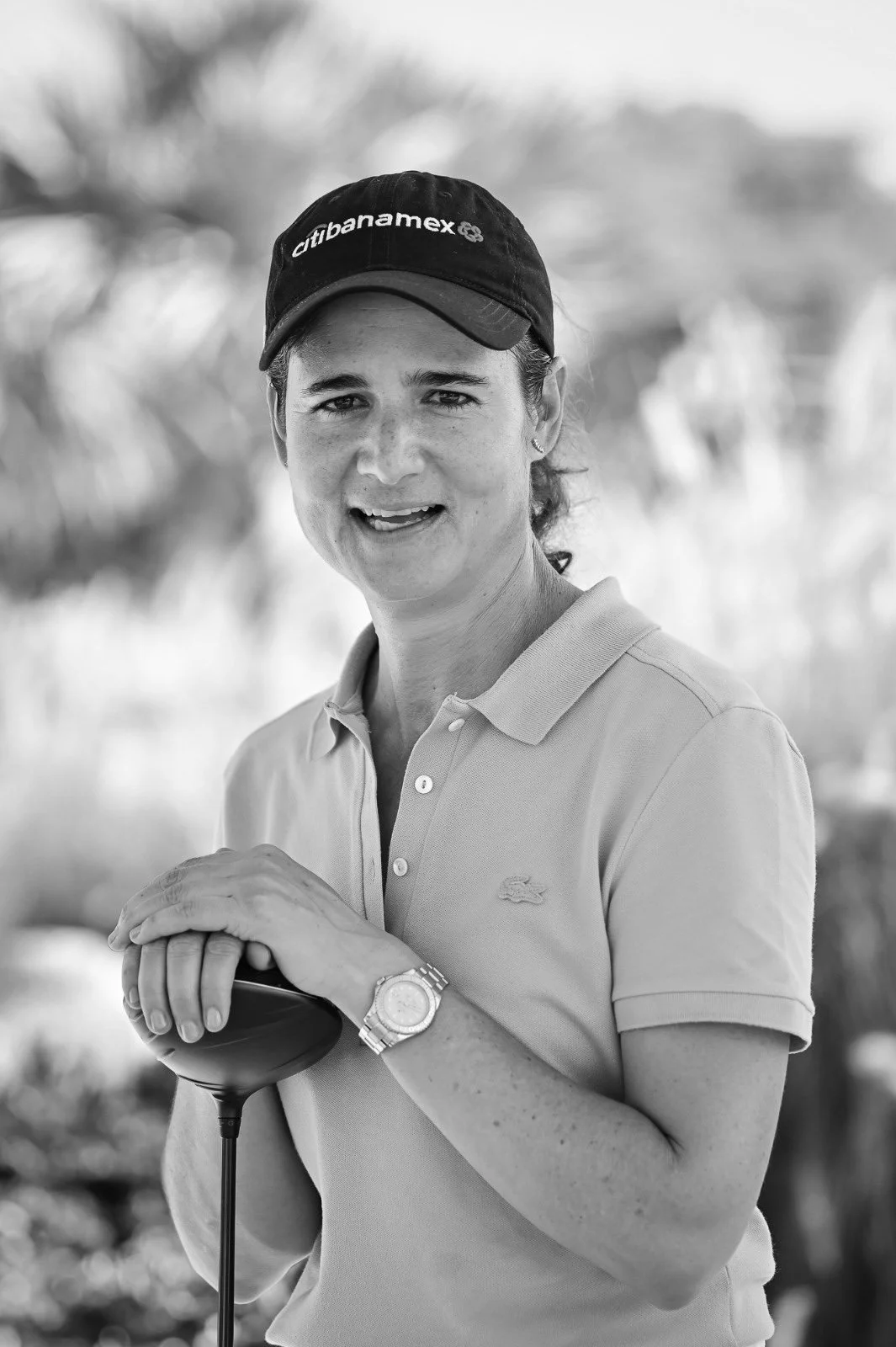 Mujer con gorra y polo sosteniendo un palo de golf en un entorno exterior.