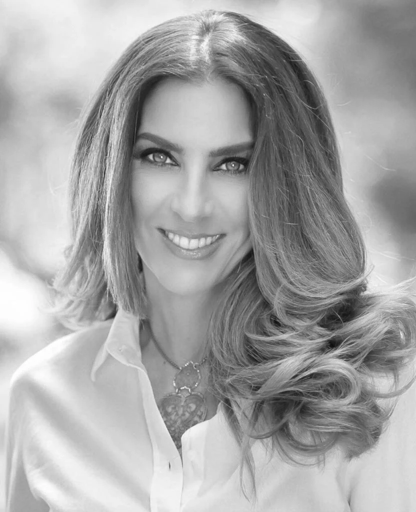 Retrato en blanco y negro de una mujer sonriendo con cabello largo y rizado, vestida con blusa blanca y collar.
