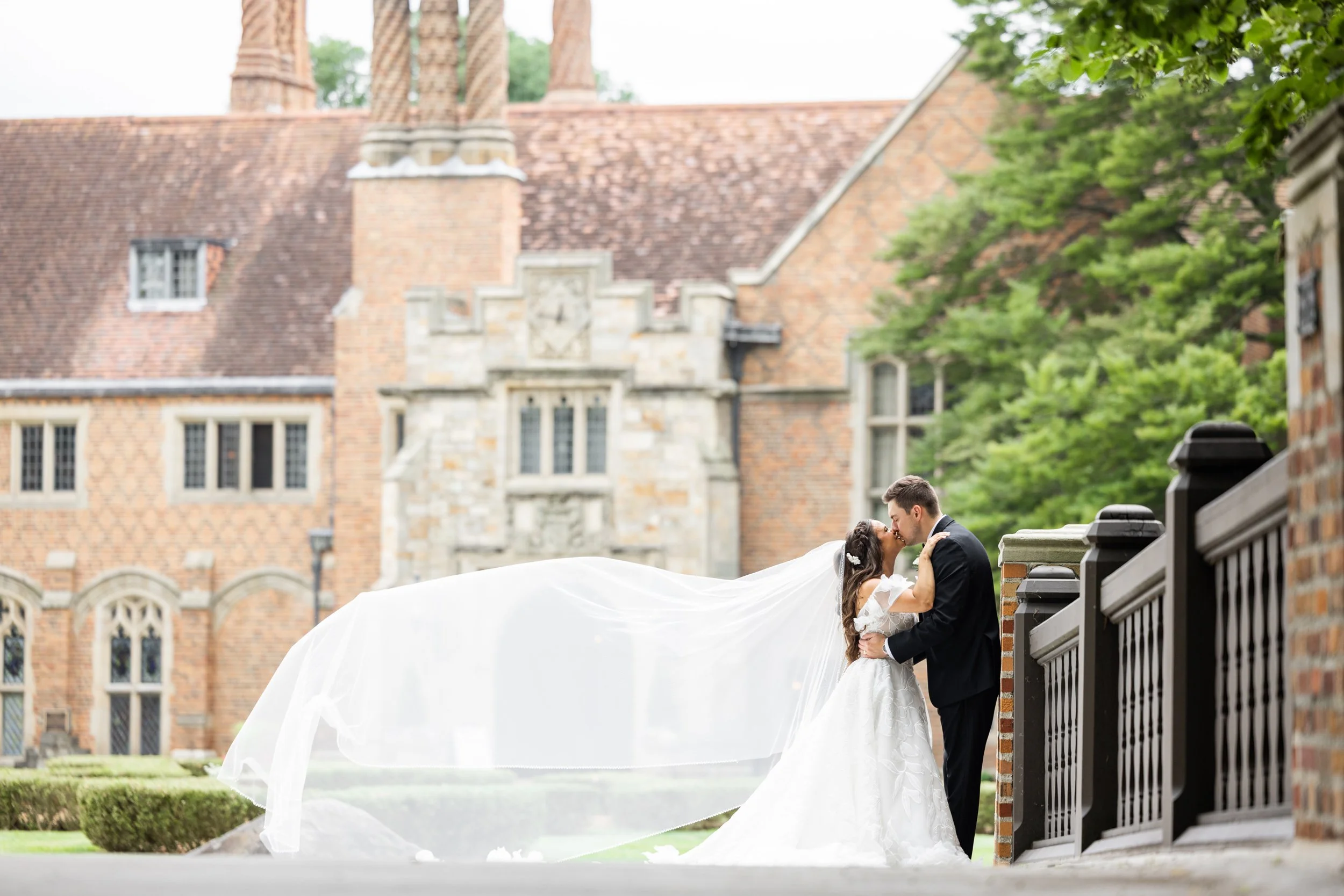 Bride and groom kiss with veil blowing outside Meadow Brook Hall in Rochester, Michigan