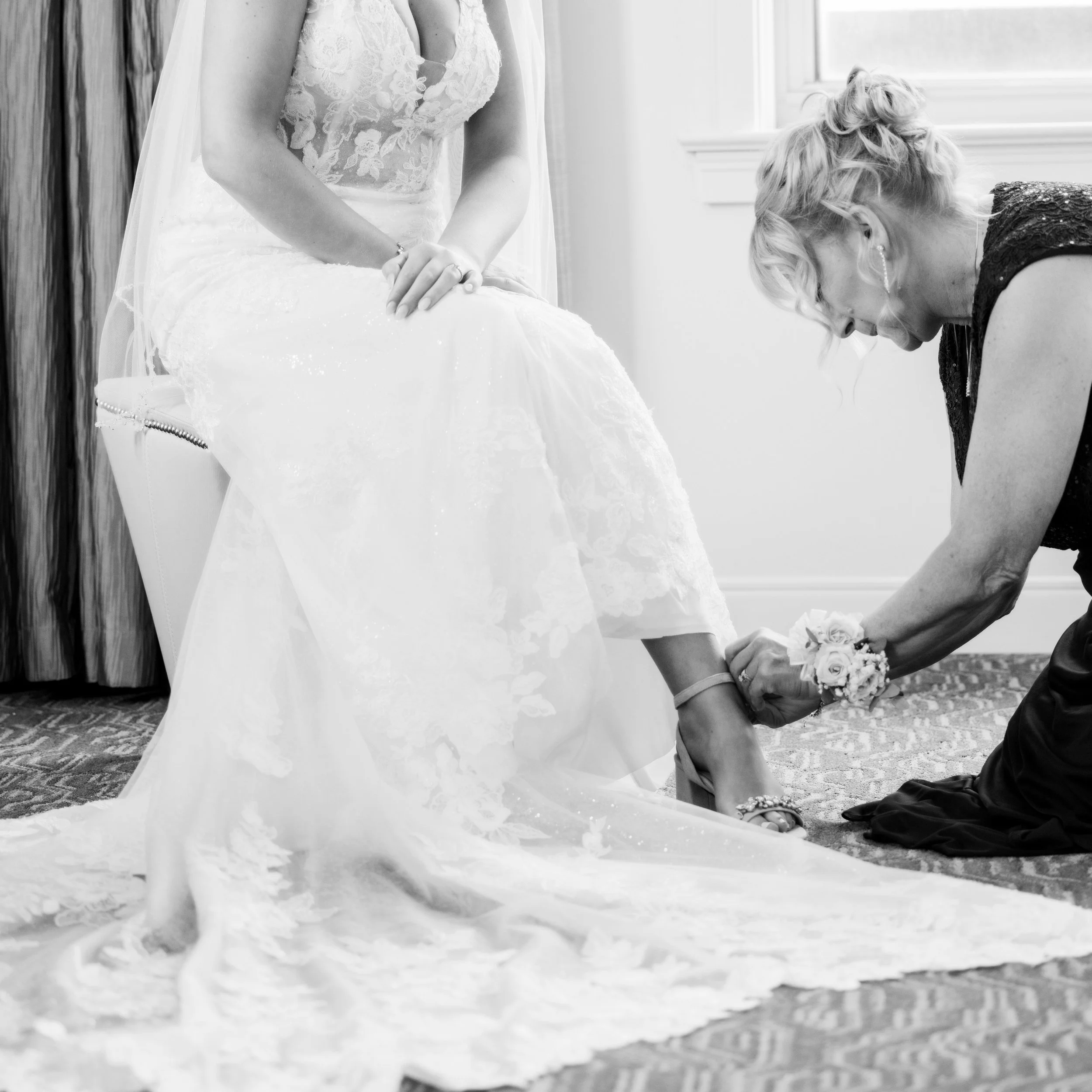 Wedding photography of a mother of bride helping her daughter put on her shoe before a Birmingham, Michigan ceremony