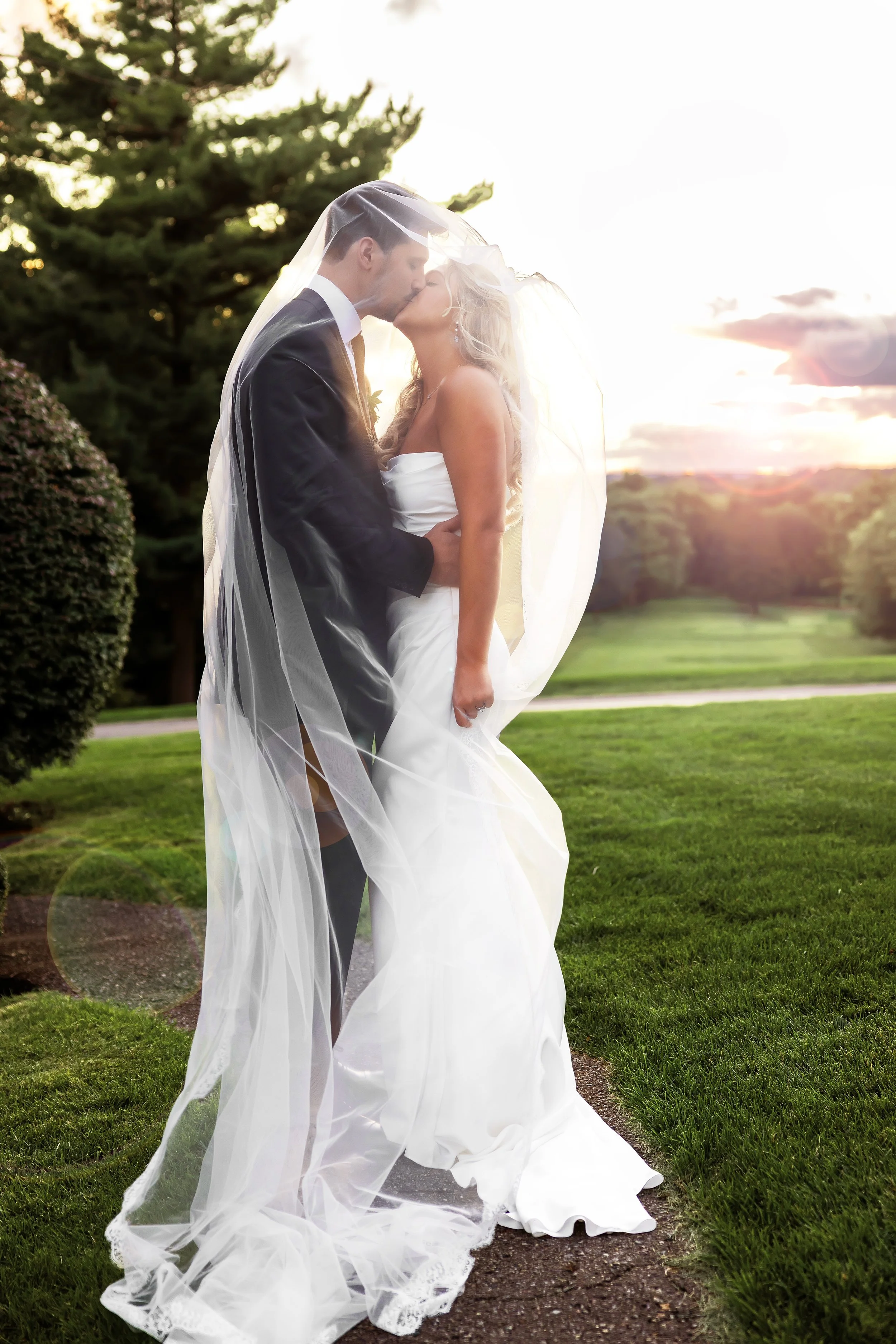 bride and groom kissing under veil during golden hour at pine knob mansion in clarkston, michigan