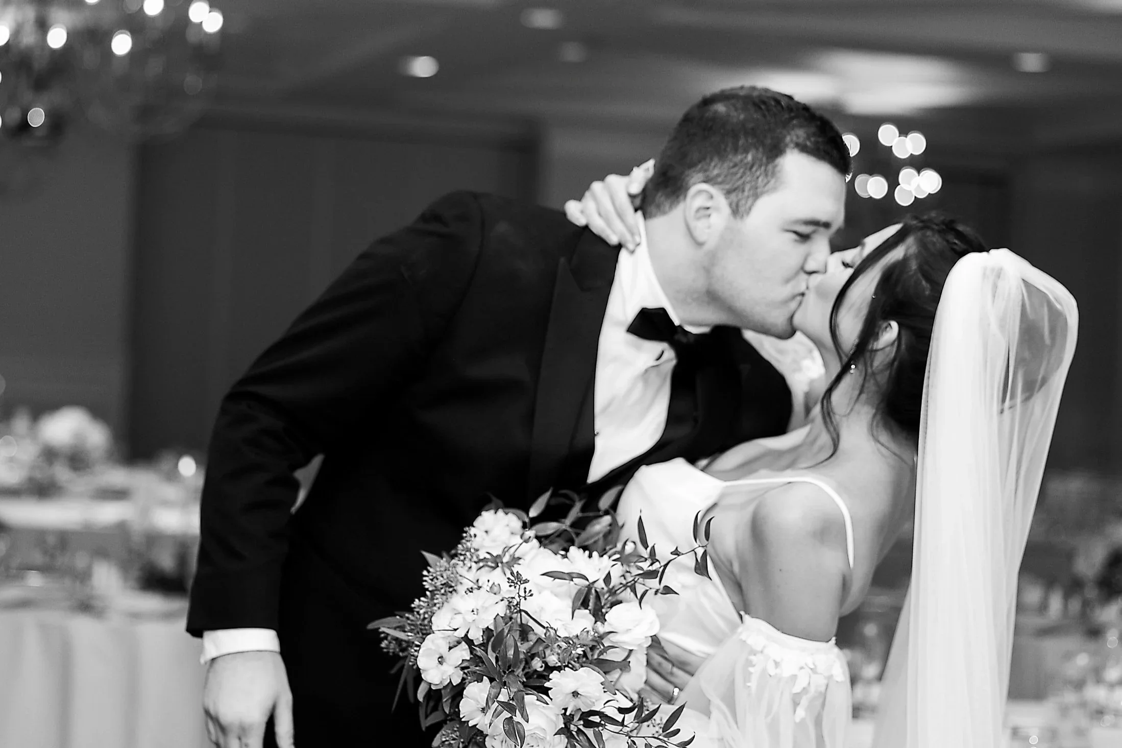 black and white wedding photo of bride and groom kissing at reception