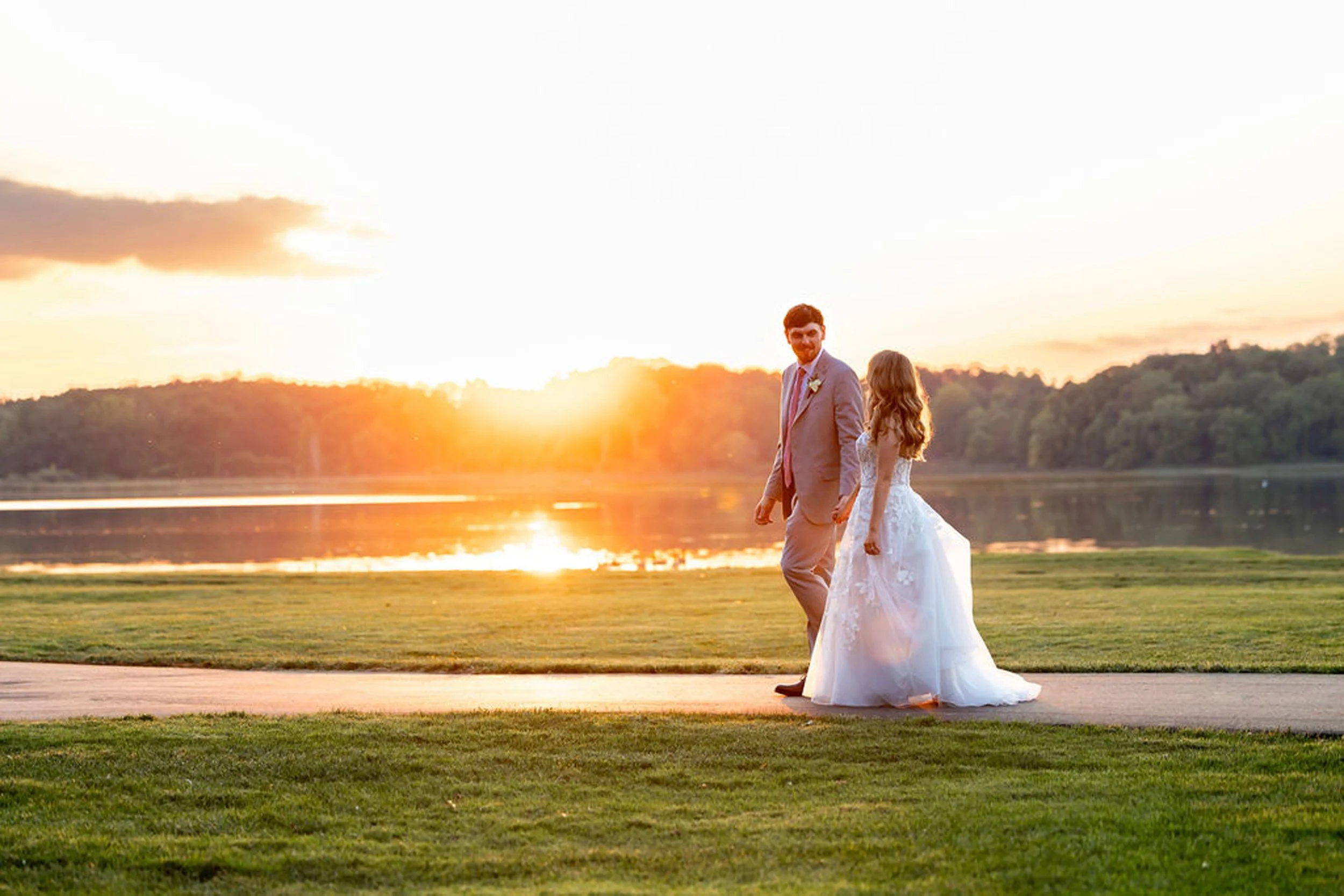 Bride and groom walk in front of sunset at Waldenwoods