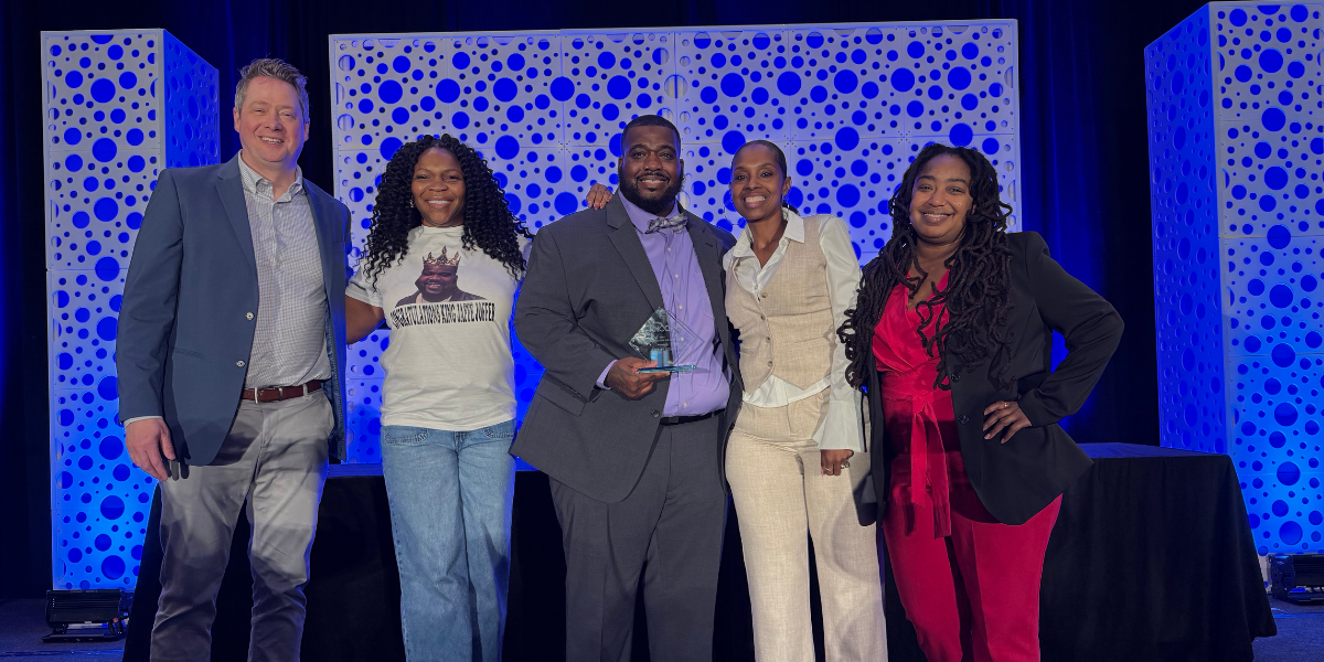 Jeromy holding his award while standing in the middle of SJCS team members