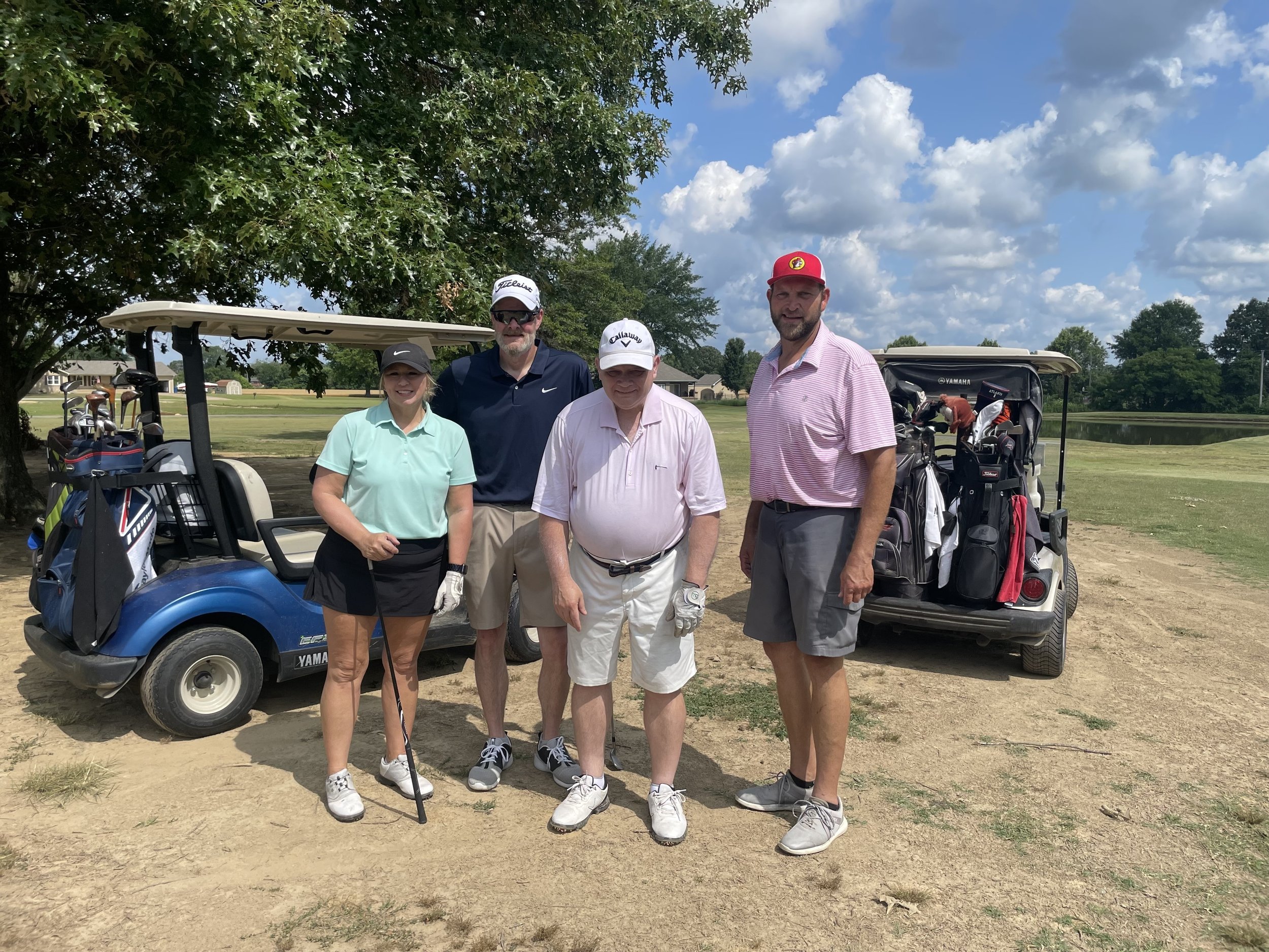 A group of golfers standing next to each other, in front of golf carts outside.
