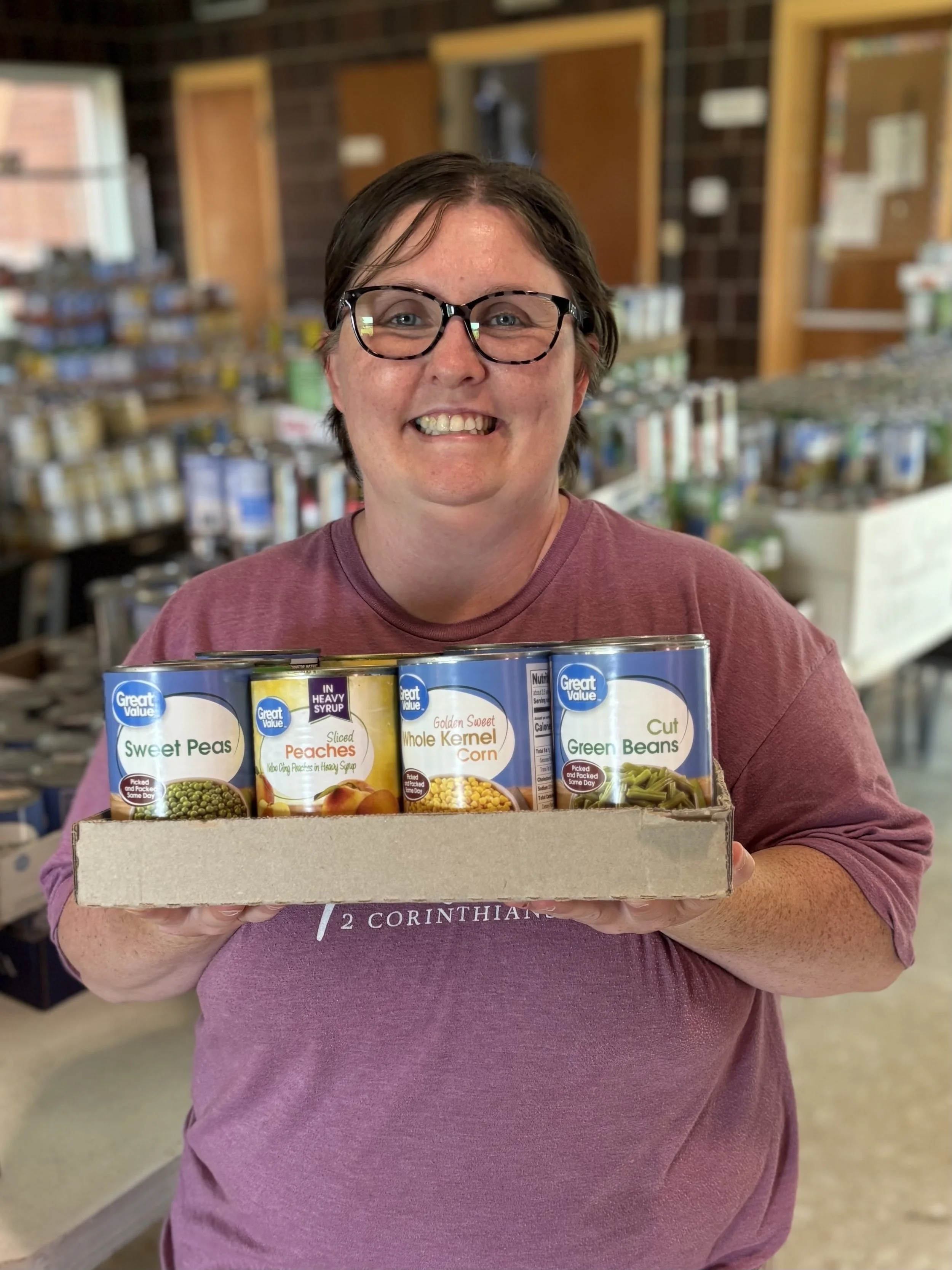 A photo of Faye, one of the people we support, who is holding a box of canned goods from our food pantry.