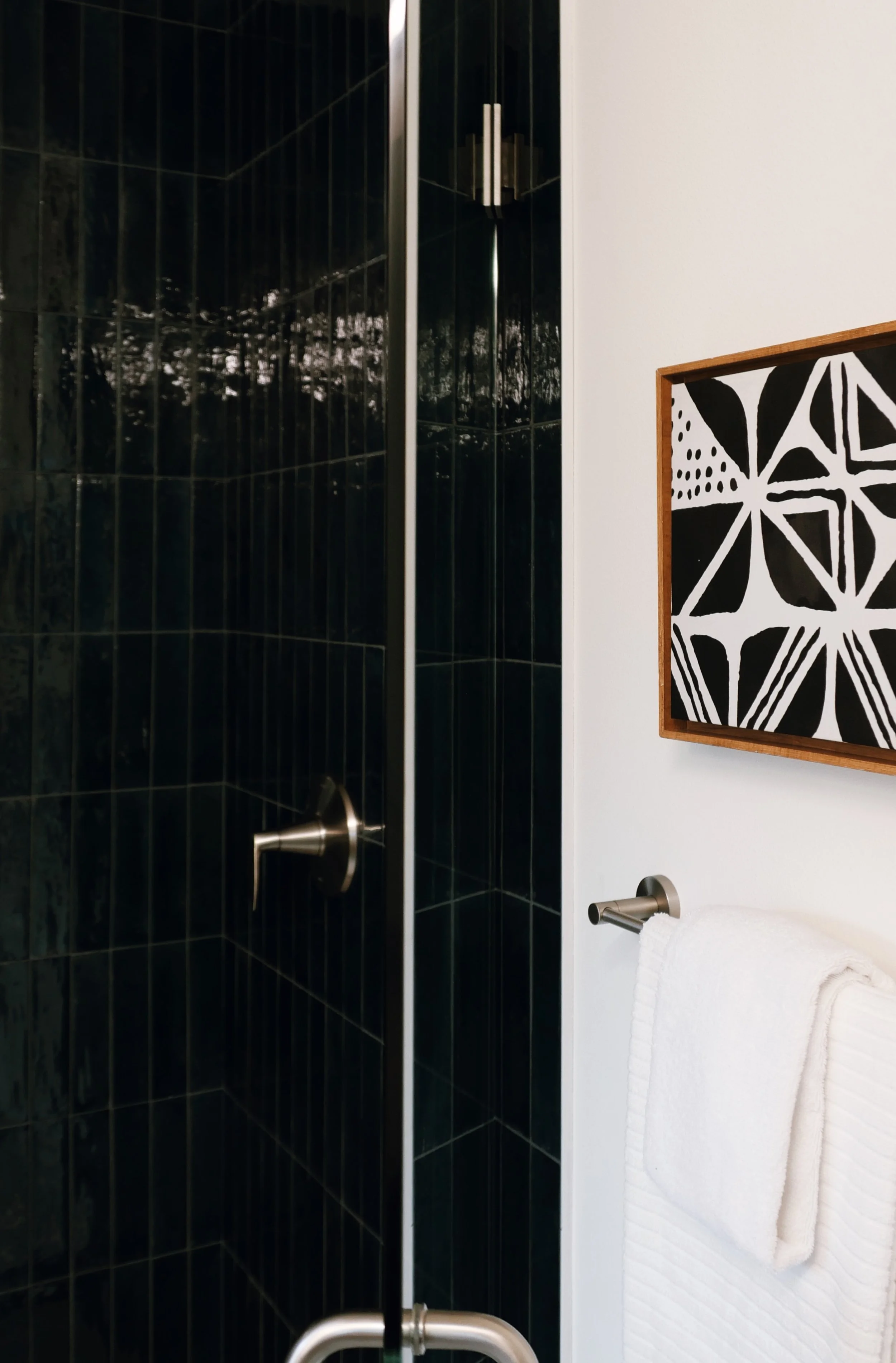 Close-up of a black-tiled shower with a bathroom wall-mounted towel rack holding a white towel and a decorative black-and-white framed artwork on the white wall.