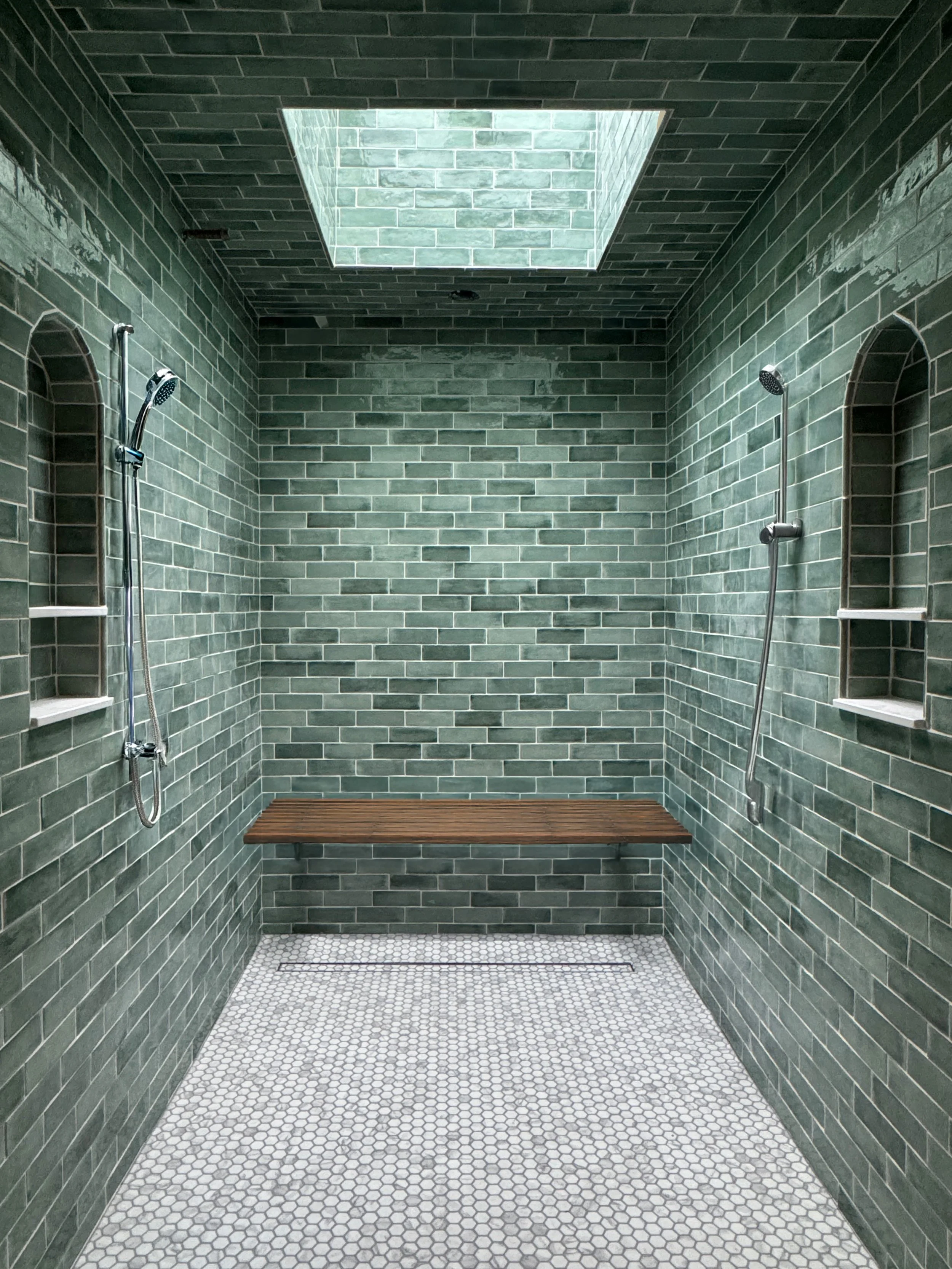 A modern walk-in shower with green subway tile walls, a skylight overhead, a wooden bench, and built-in shelves in the walls.