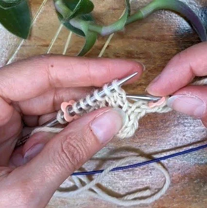 two hands hold a swatch of fabric indicating the stitch to pick up for a right lifted increase.