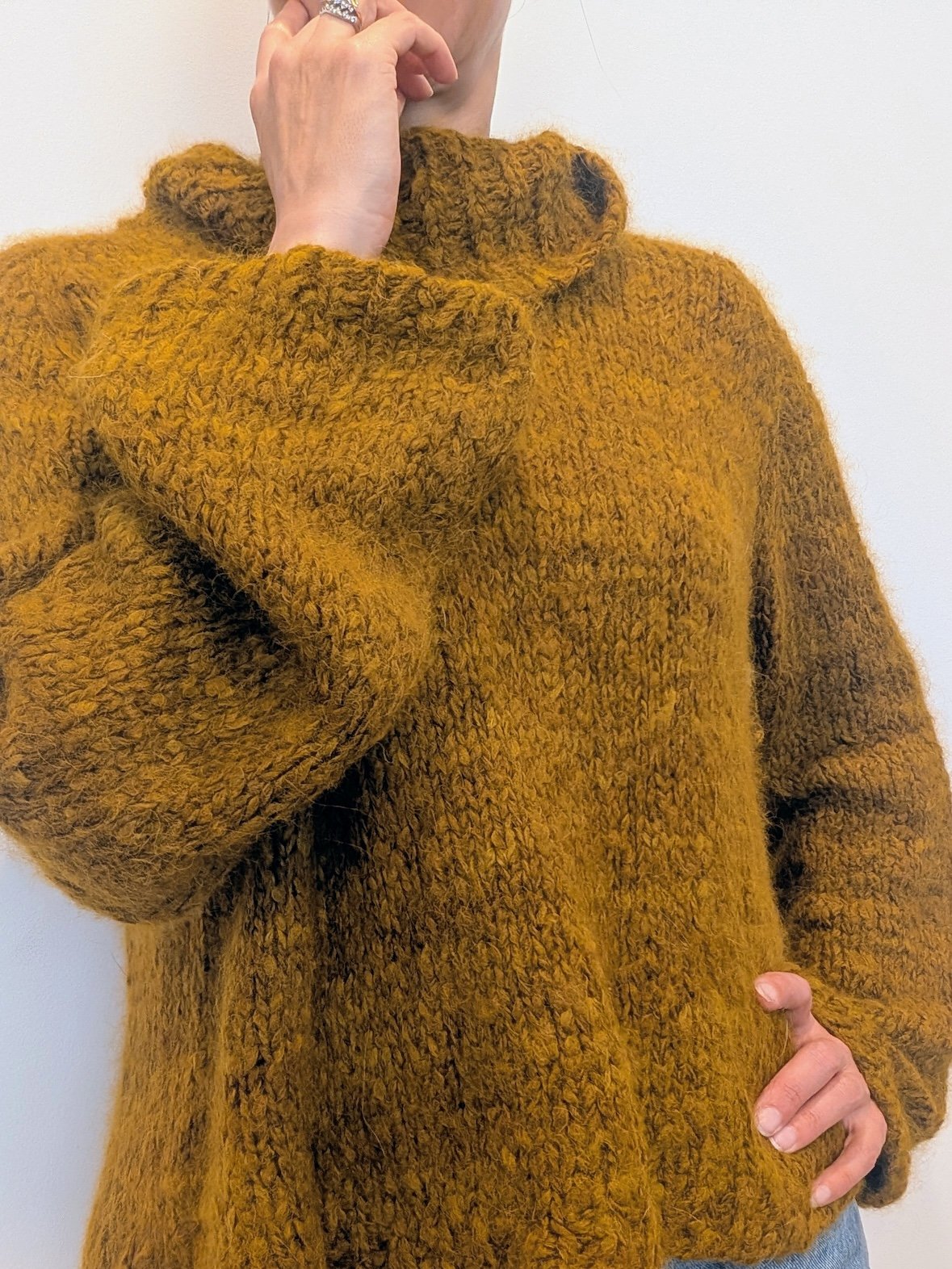 the torso of a woman is shown wearing an olive green drapey sweater.