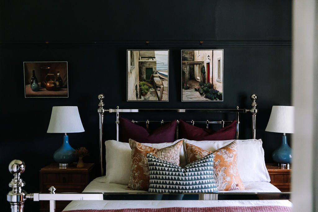  AFTER: The master bedroom is now an inviting, cosy haven. The mirrored bed feels right at home against a rich, dark navy backdrop which also allows the jewel tones in the accessories to pop. 