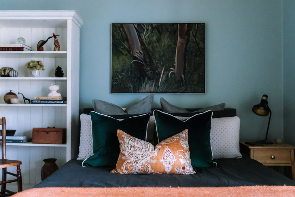  AFTER: The second guest room is a restful space and uses a lighter green-grey tone on the walls. Layers of rich textures and punches of orange and deep greens have been used in the accessories to provide further warmth and comfort. 