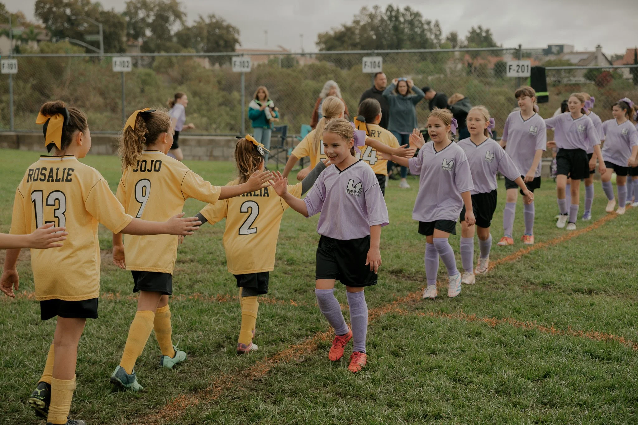 Young children playing soccer on a grass field wearing blue and yellow uniforms.