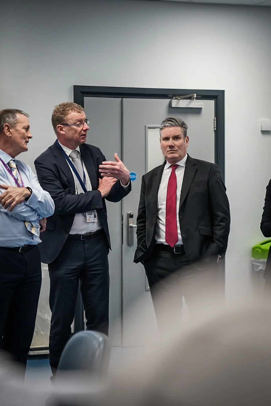 Three men in business suits having a discussion in an office room, with a door in the background.