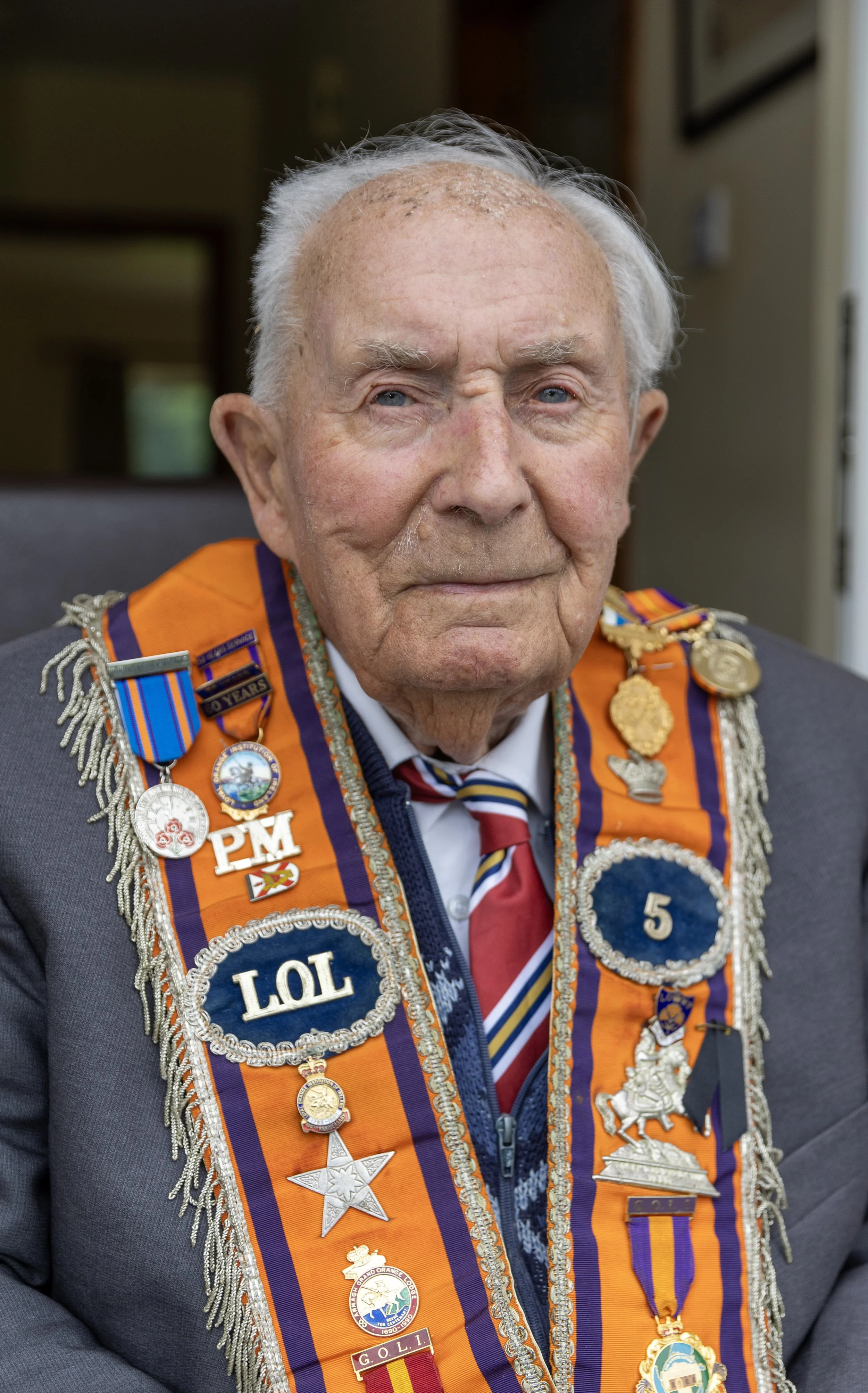 An elderly man wearing a dark suit and multiple military medals and badges across his chest. He has white hair, blue eyes, and a proud expression.