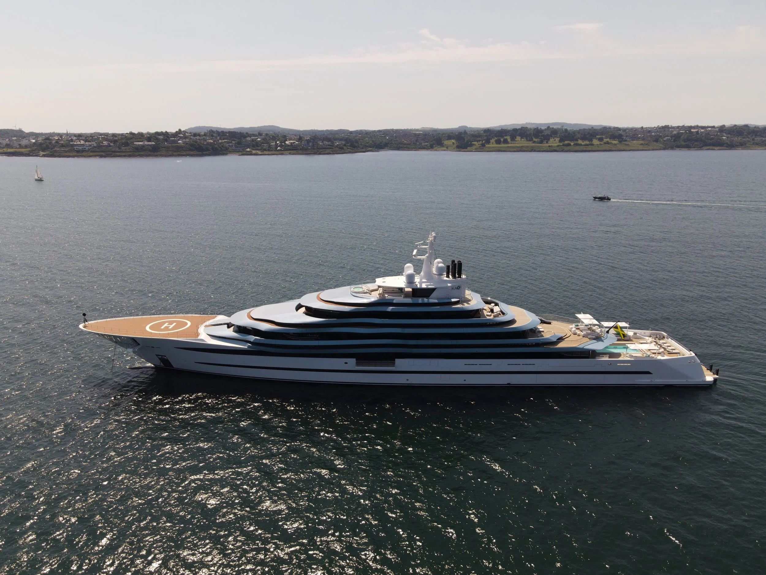 A large modern luxury yacht sailing in calm waters with a coastline in the background.
