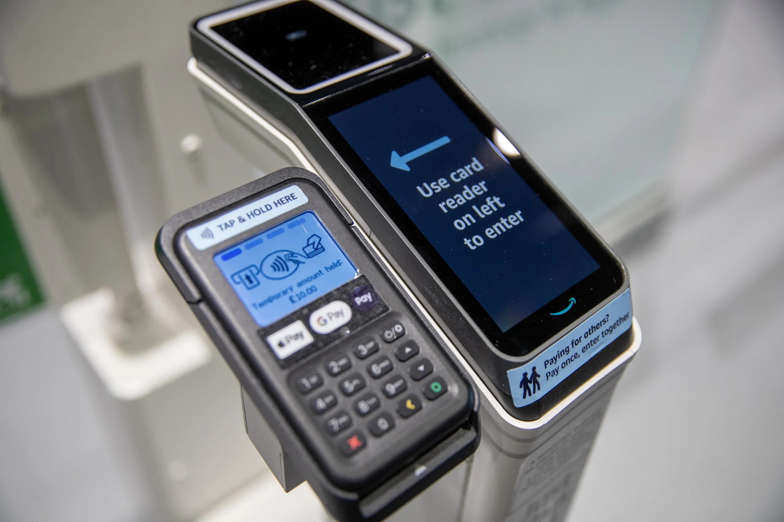 Contactless payment terminals, including a card reader and a mobile device, at a checkout point with instructions to use the card reader on the left to enter.