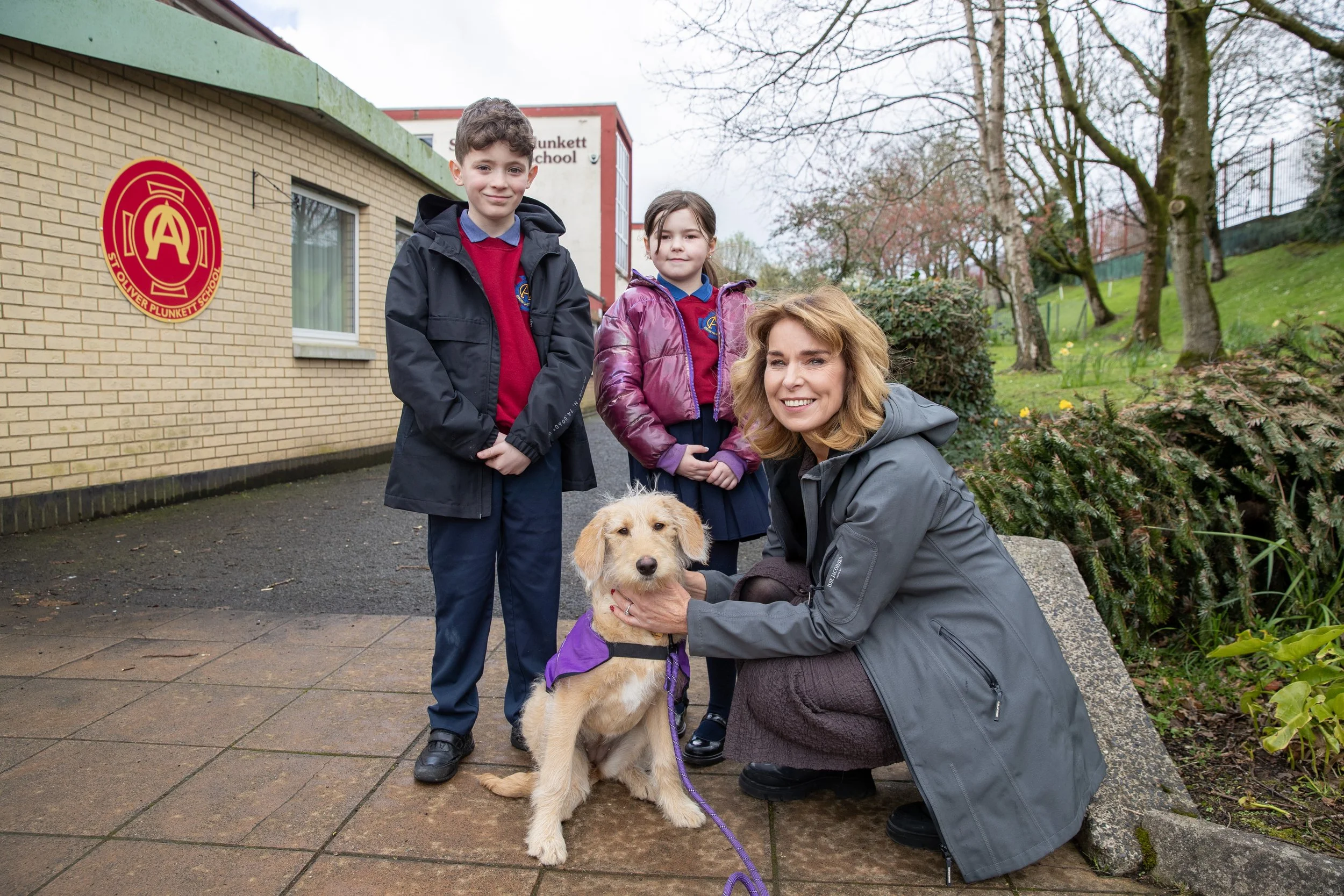 A woman with two children and a guide dog outside a school building.