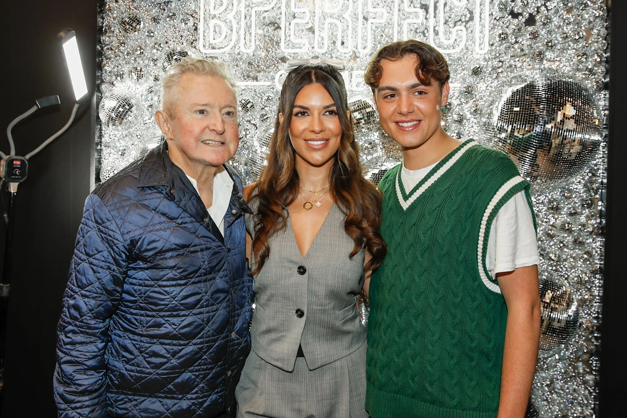 Three people standing together smiling at a decorated event with silver disco balls and a sign in the background that says 'BFFER' or similar.