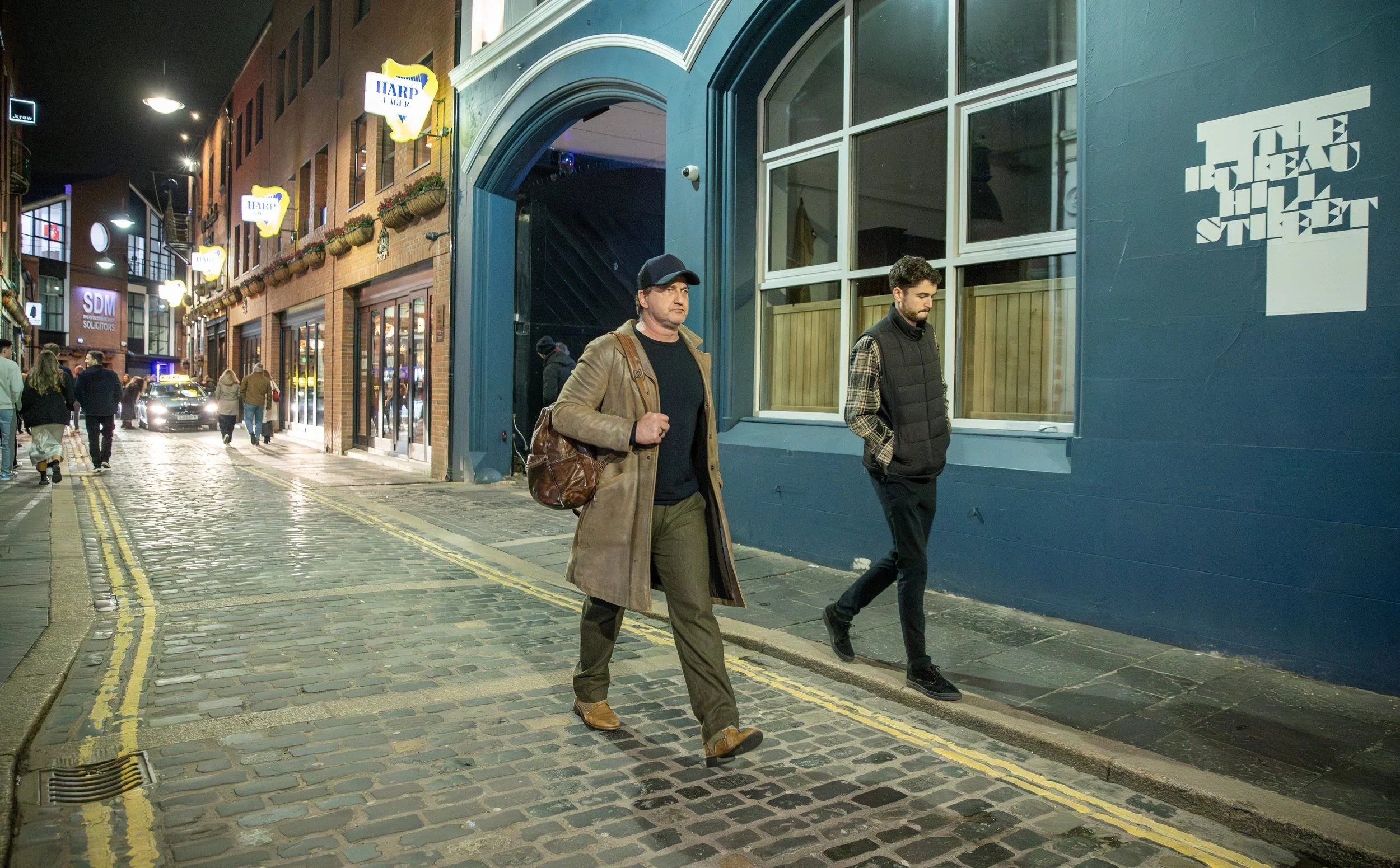 People walking on a cobblestone street at night, with shops and illuminated signs along the sidewalk.