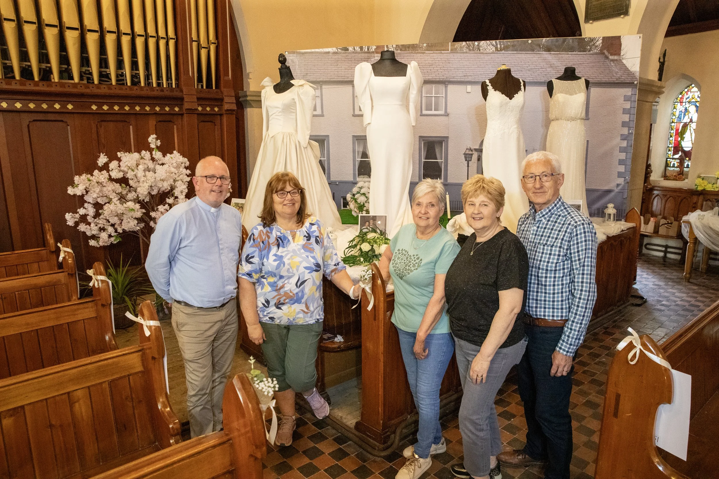 A group of five people posing inside a church next to a display of wedding dresses on mannequins