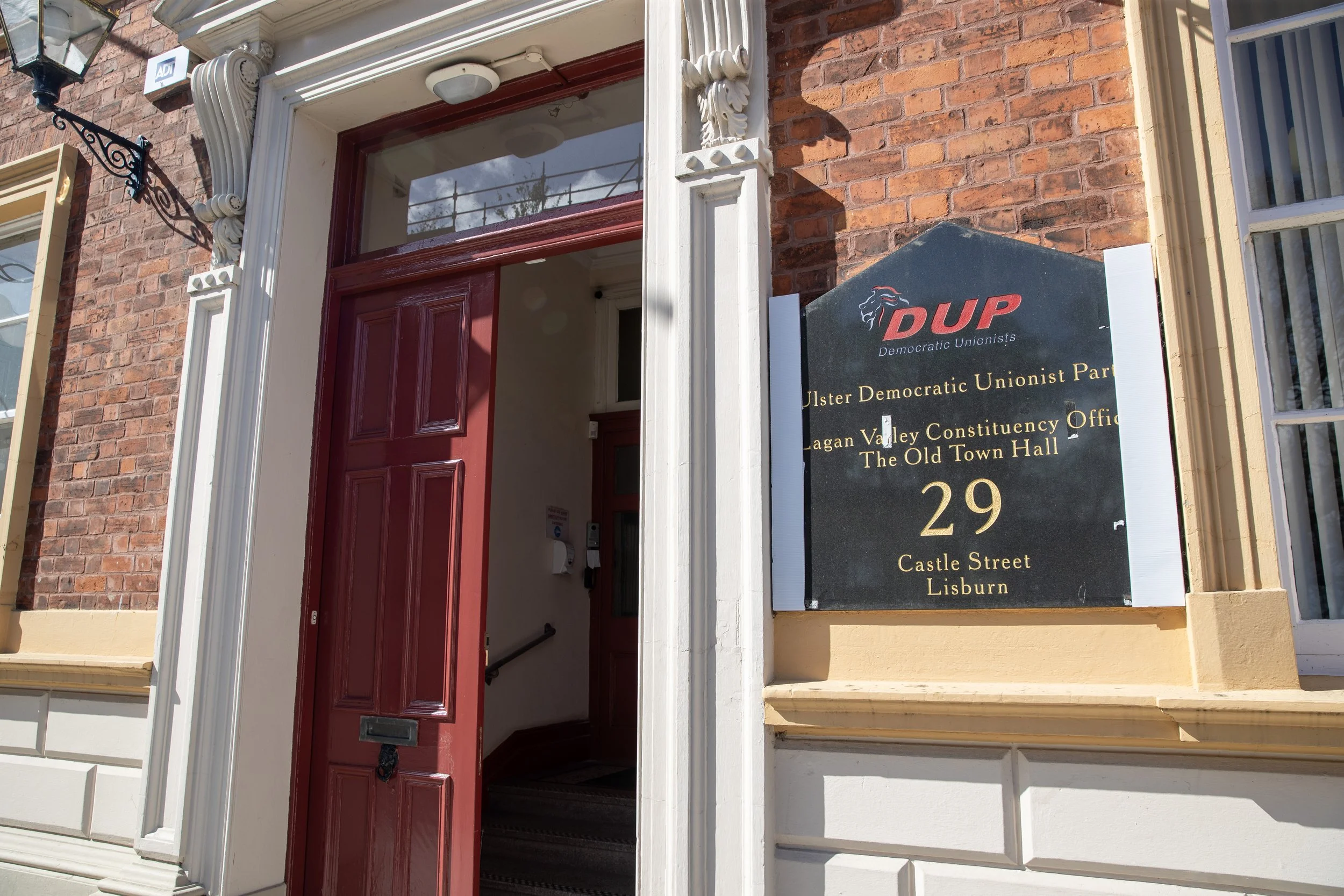 Building entrance with a red door and a black sign on the wall reads 'Ulster Democratic Unionist Party, Lagan Valley Constituency Office, The Old Town Hall, 29 Castle Street, Lisburn.'
