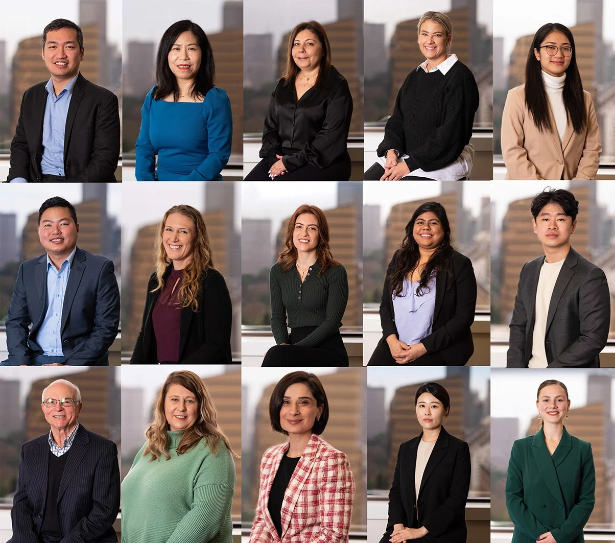 Group portrait of 15 diverse professionals in business attire, poses for a corporate team photo with cityscape background.
