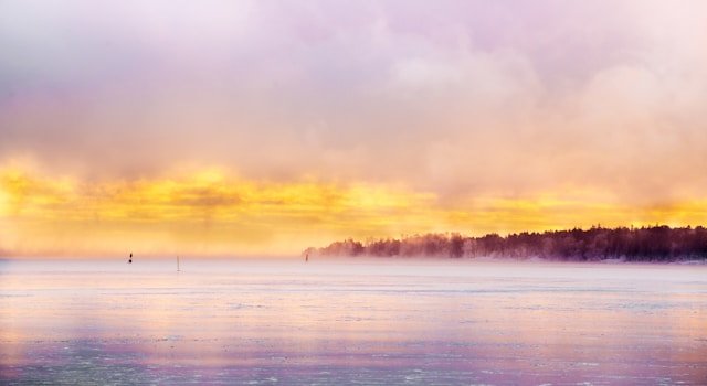 Colorful sunrise over a misty frozen lake with trees in the distance.