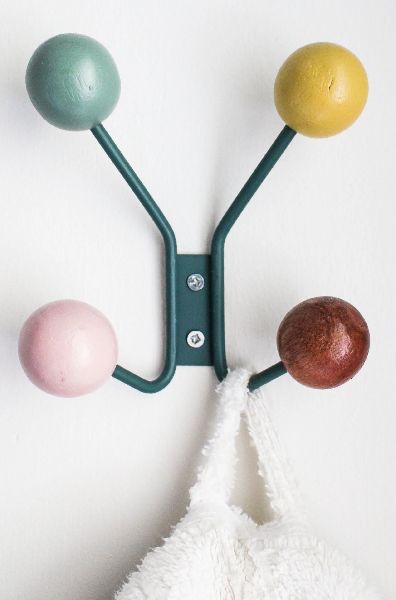 Decorative coat rack with four colorful wooden balls on metal hooks, holding a white towel.