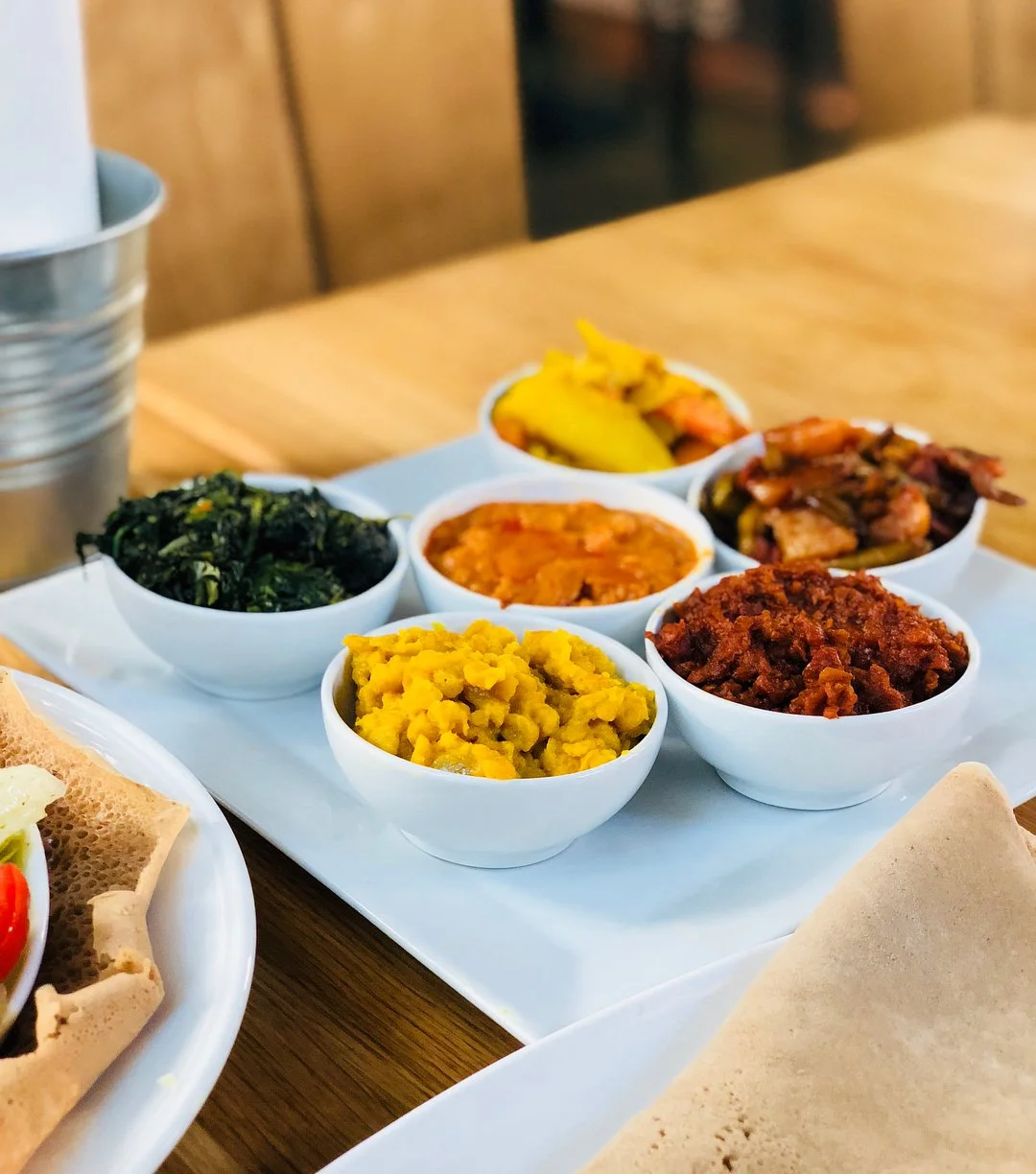 Brett med små vita skålar fyllda med olika sorters eritreanska rätter och grönsaker, samt en tallrik med injera.
