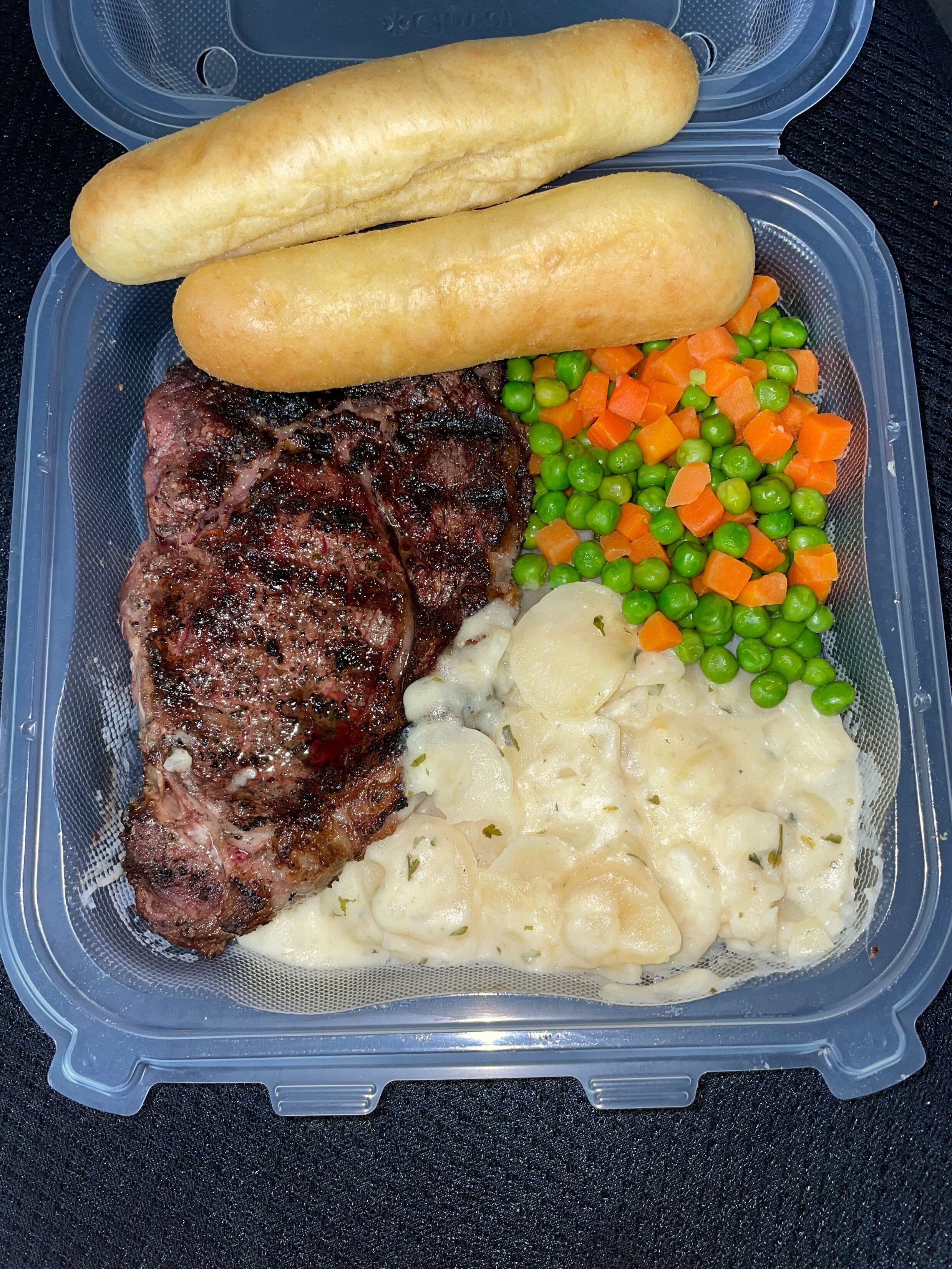 Grilled Rib Eye Steak, Scalloped Potatoes, Peas and Carrots with Bread Sticks.