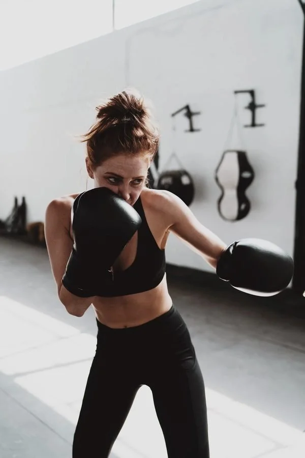 Woman in sportswear and boxing gloves practicing boxing moves.
