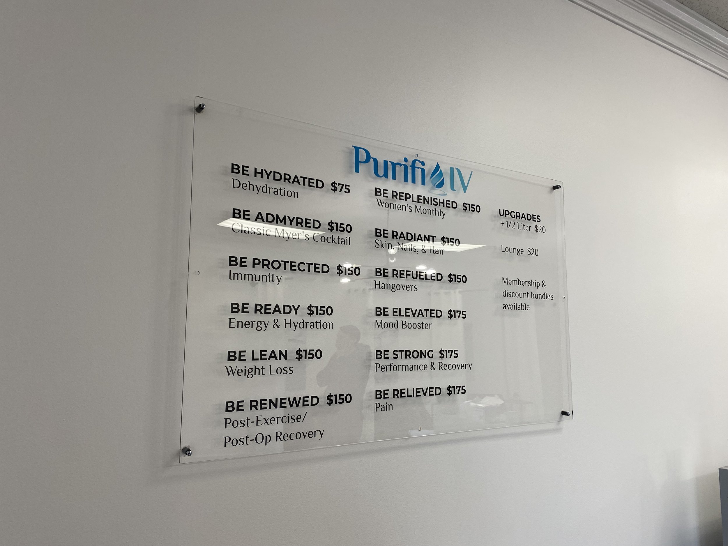 A wall-mounted menu board for Purifi IV with various intravenous hydration options listed along with prices. Categories include hydration, immunity, energy and hydration, weight loss, and recovery among others. Prices range from $75 to $175, with add