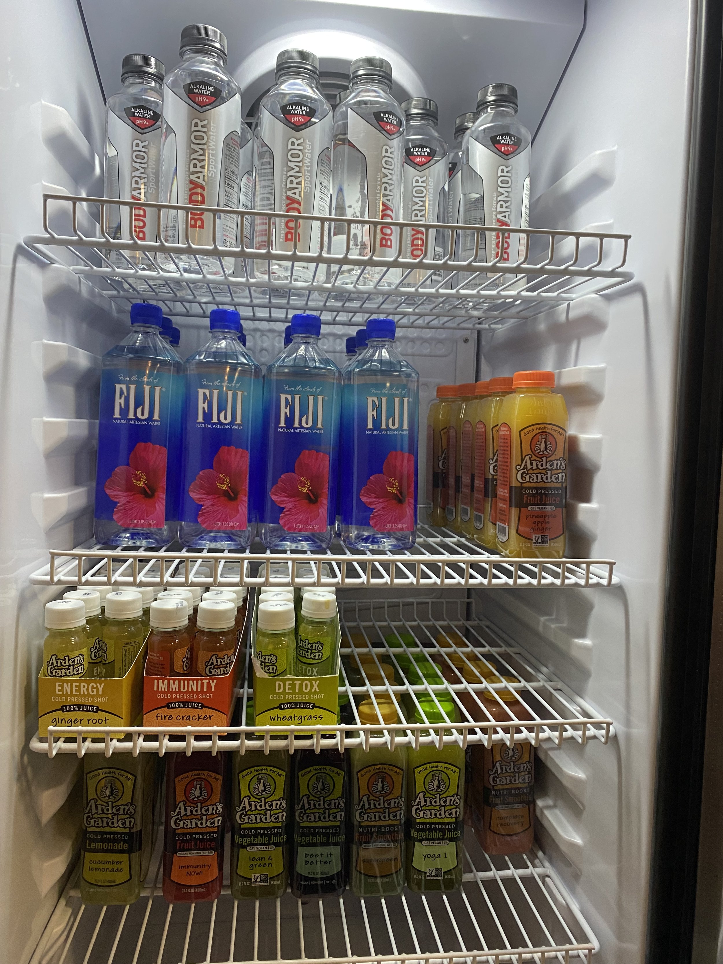 Refrigerator stocked with bottles of BodyArmor sports water, Fiji water, and Arden's Garden juices and cold-pressed shots.