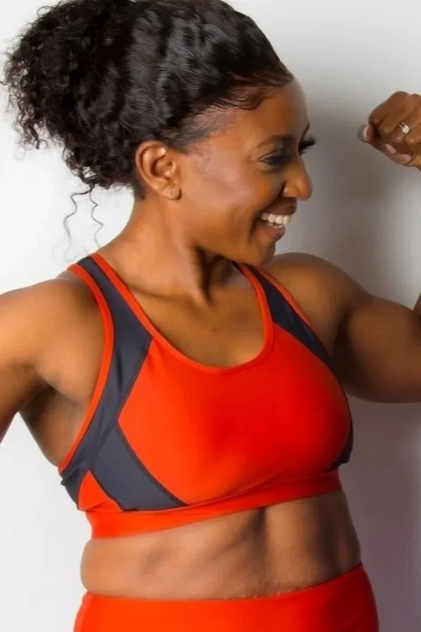 Woman flexing her arm muscles, wearing a red sports bra and smiling.