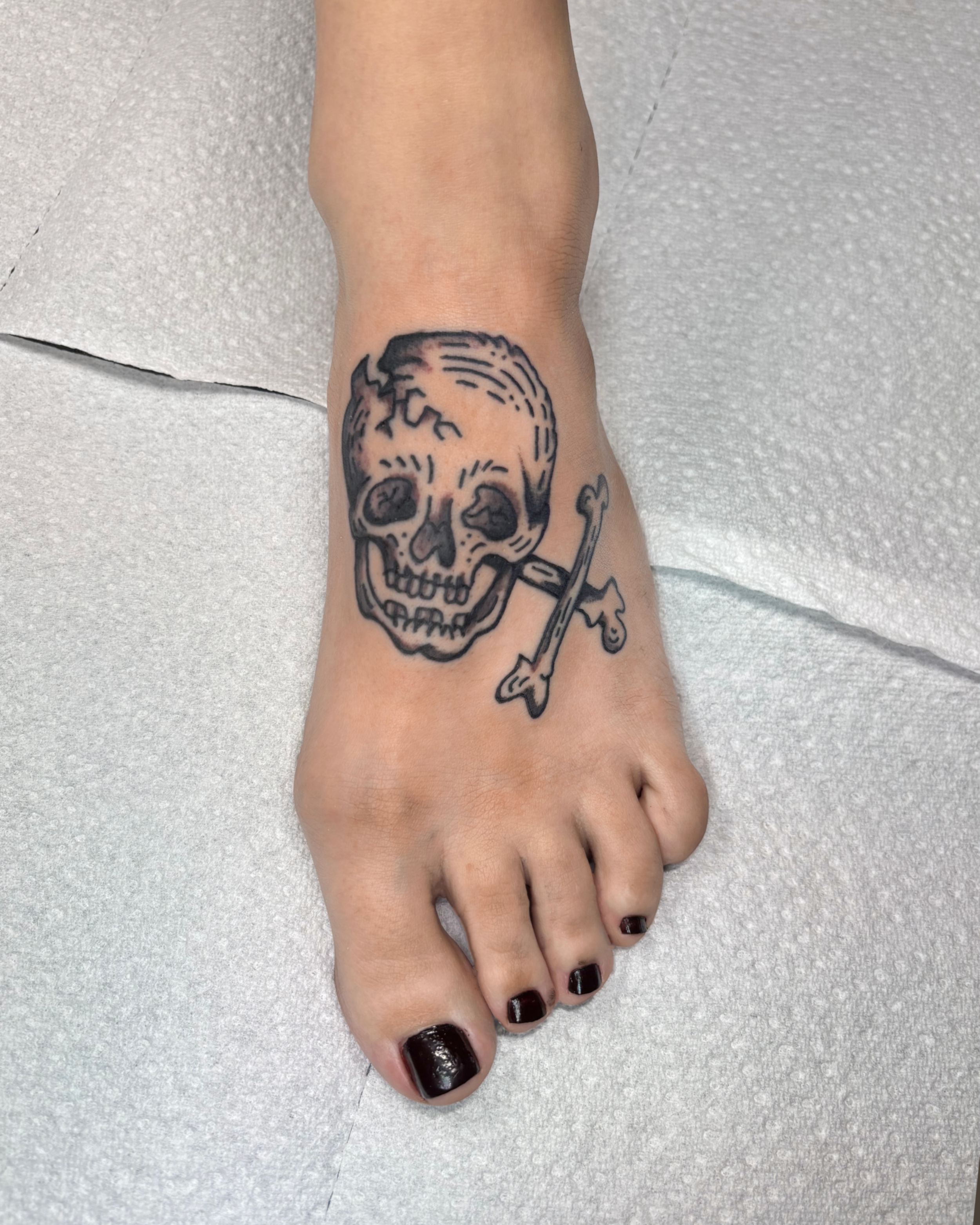 Tattoo of a skull and crossbones on a person's foot.