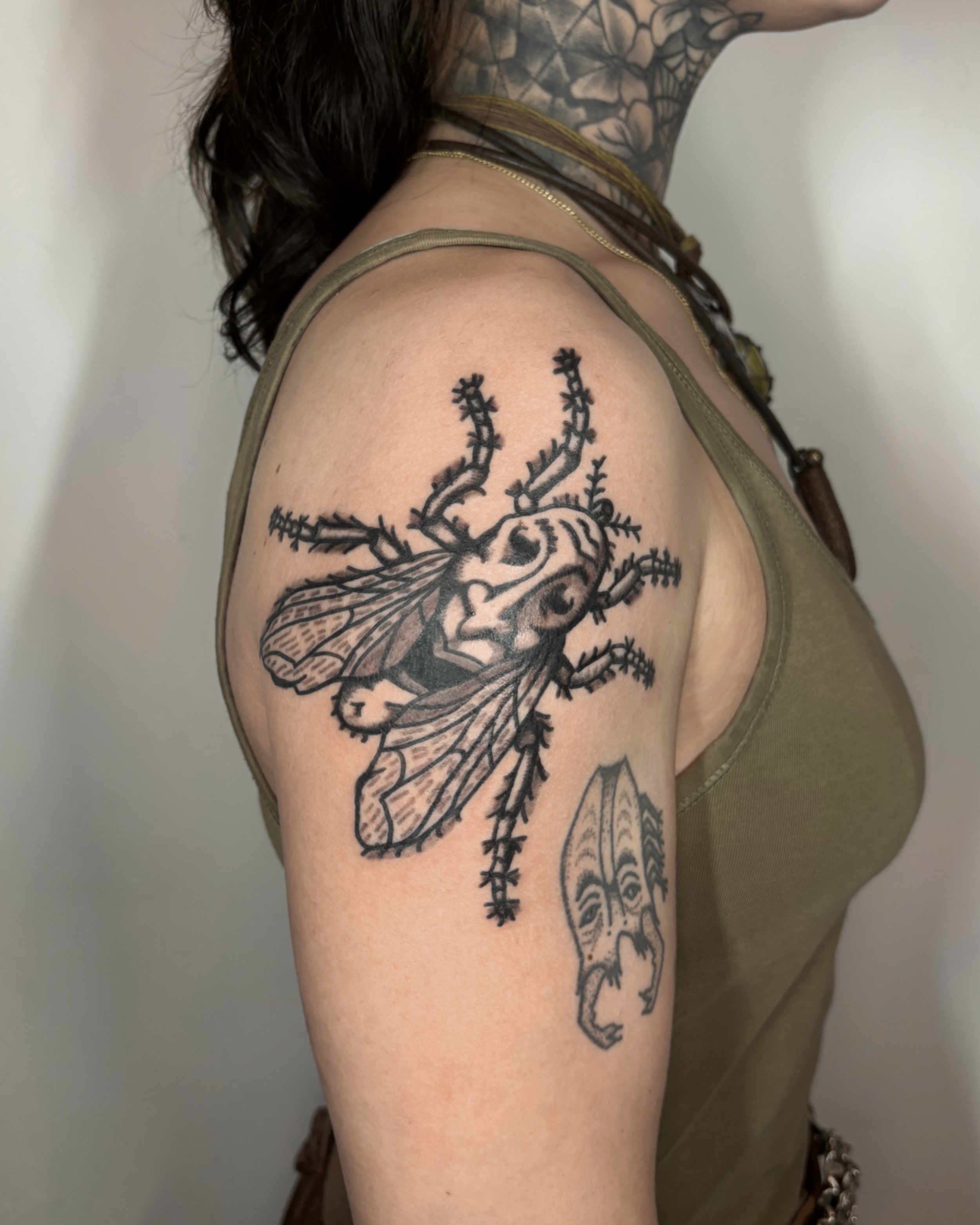 Tattoo of a bee with a skull in the middle of its body on a woman's upper arm.