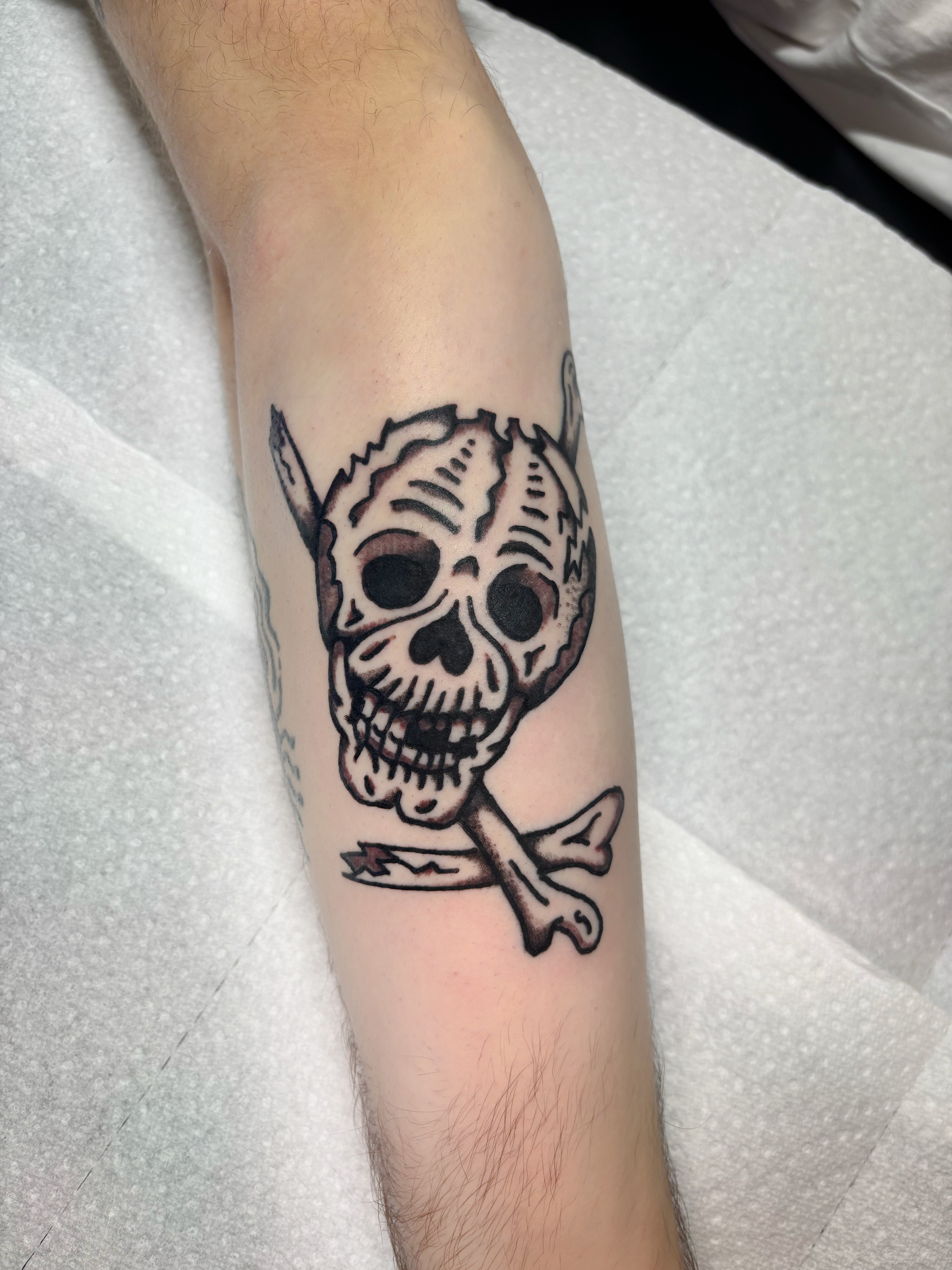Tattoo of a skull with large eye sockets and nose cavity, with a spear piercing through the top of the skull and a broken arrow crossing behind it.