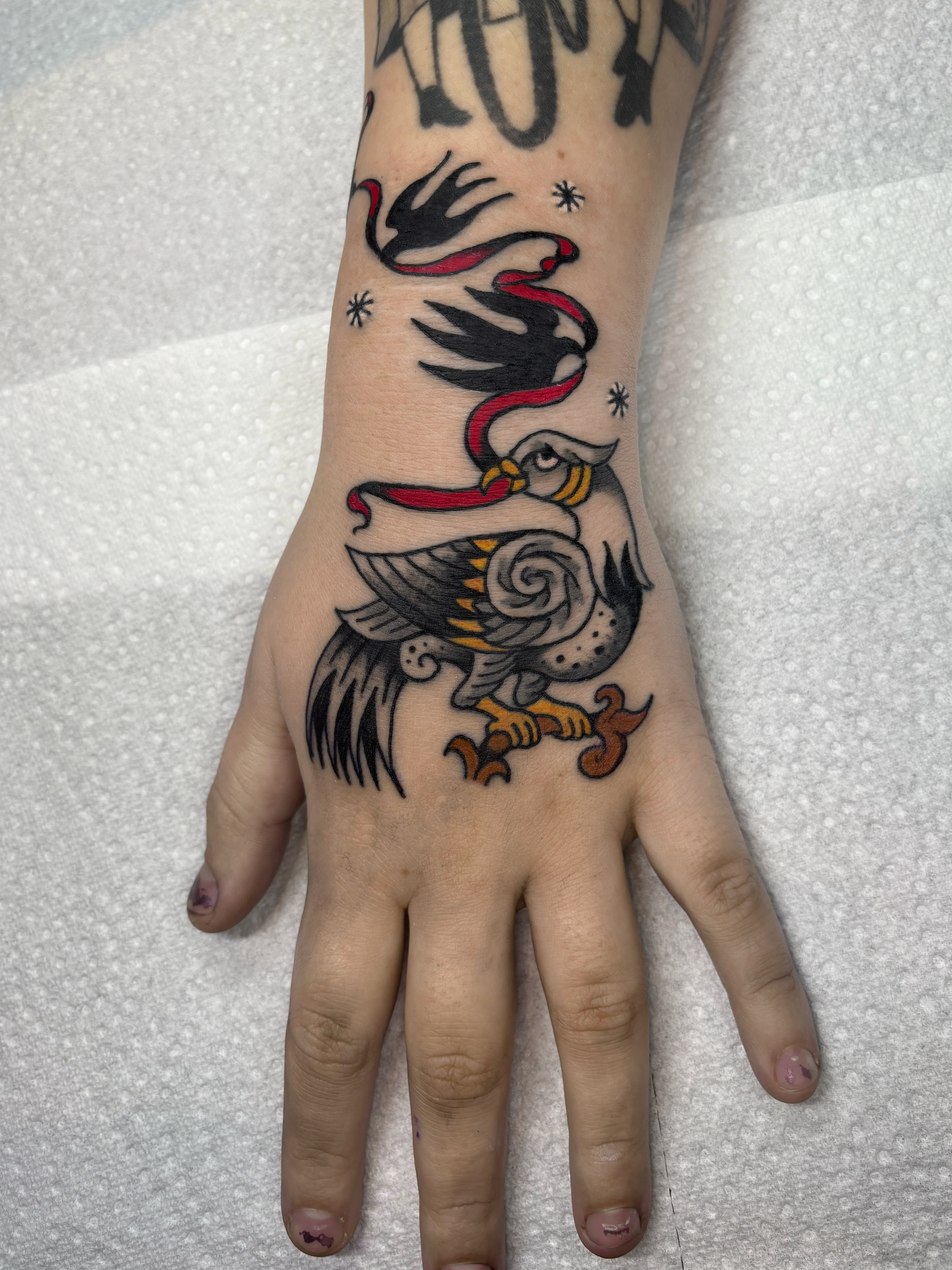 Tattoo of a stylized eagle with open wings, a spiral on its chest, and a red and black snake entwined around its neck. The tattoo is on the person's wrist.