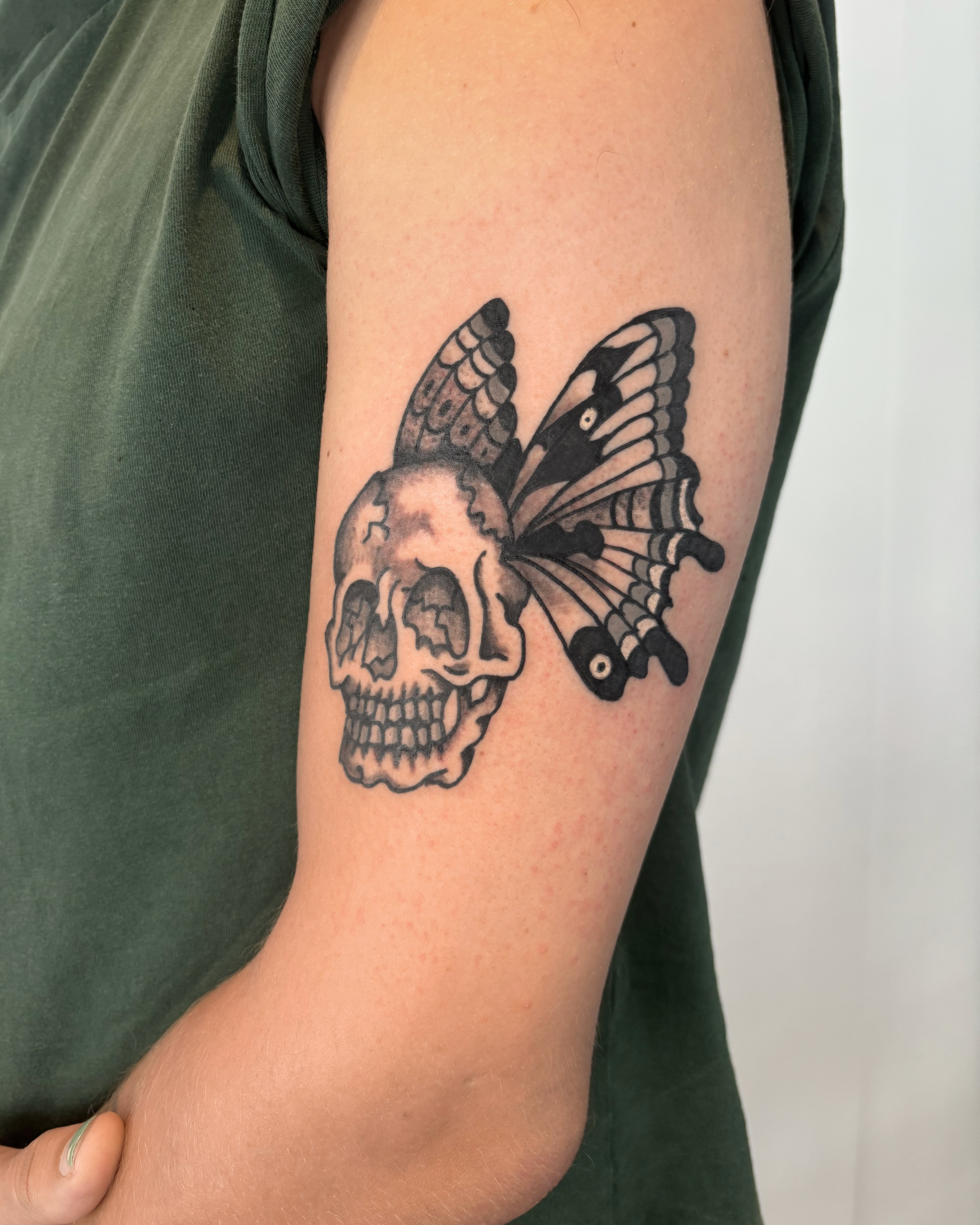 Tattoo of a skull with a butterfly wing emerging from it.