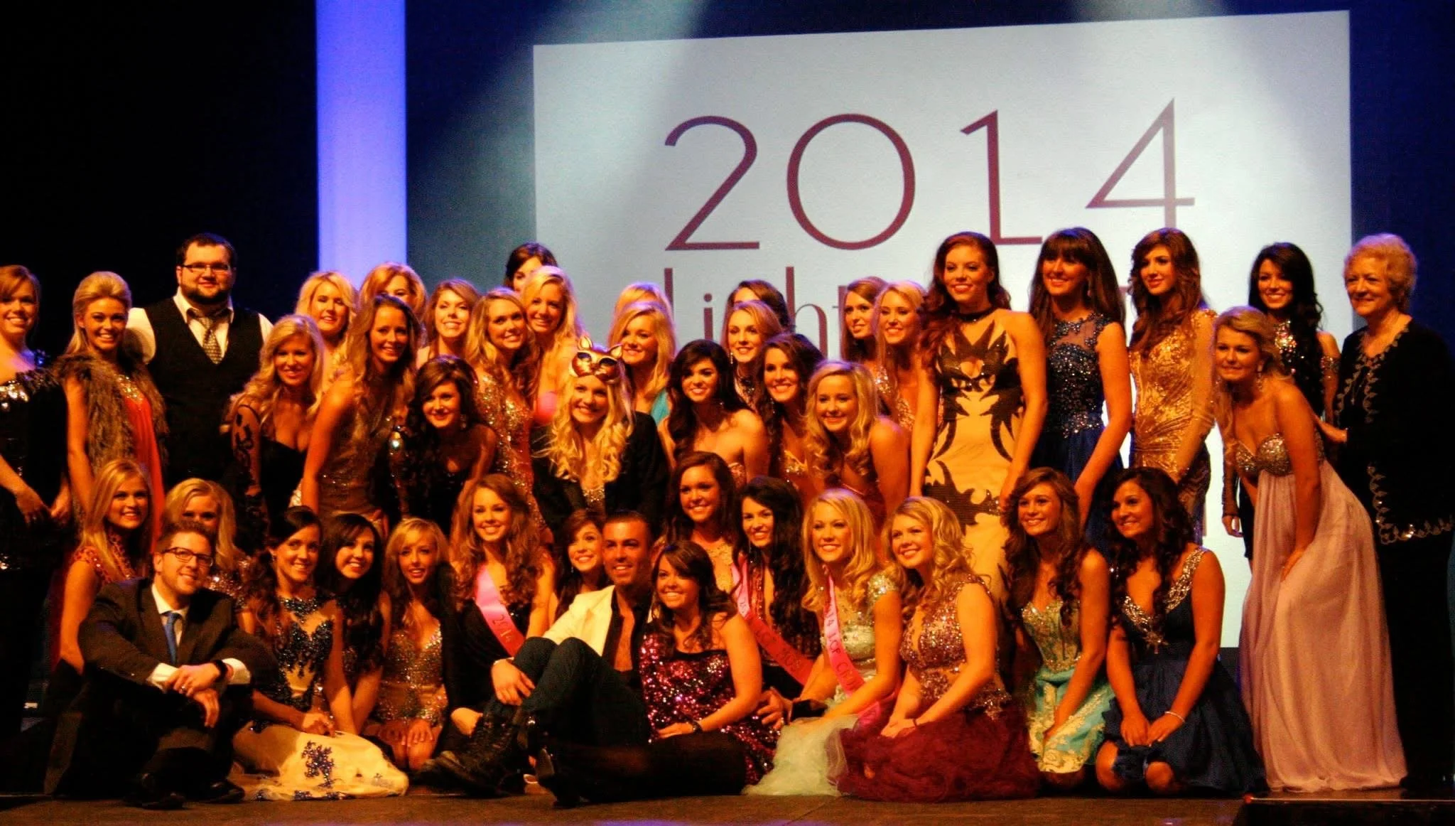 Group of women and men on stage at an event with a large screen showing the year 2014 in the background.