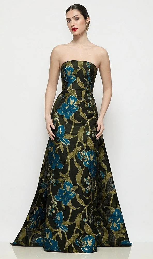 A woman wearing a strapless, floor-length black gown with a floral pattern in blue and green hues, standing against a plain white background.